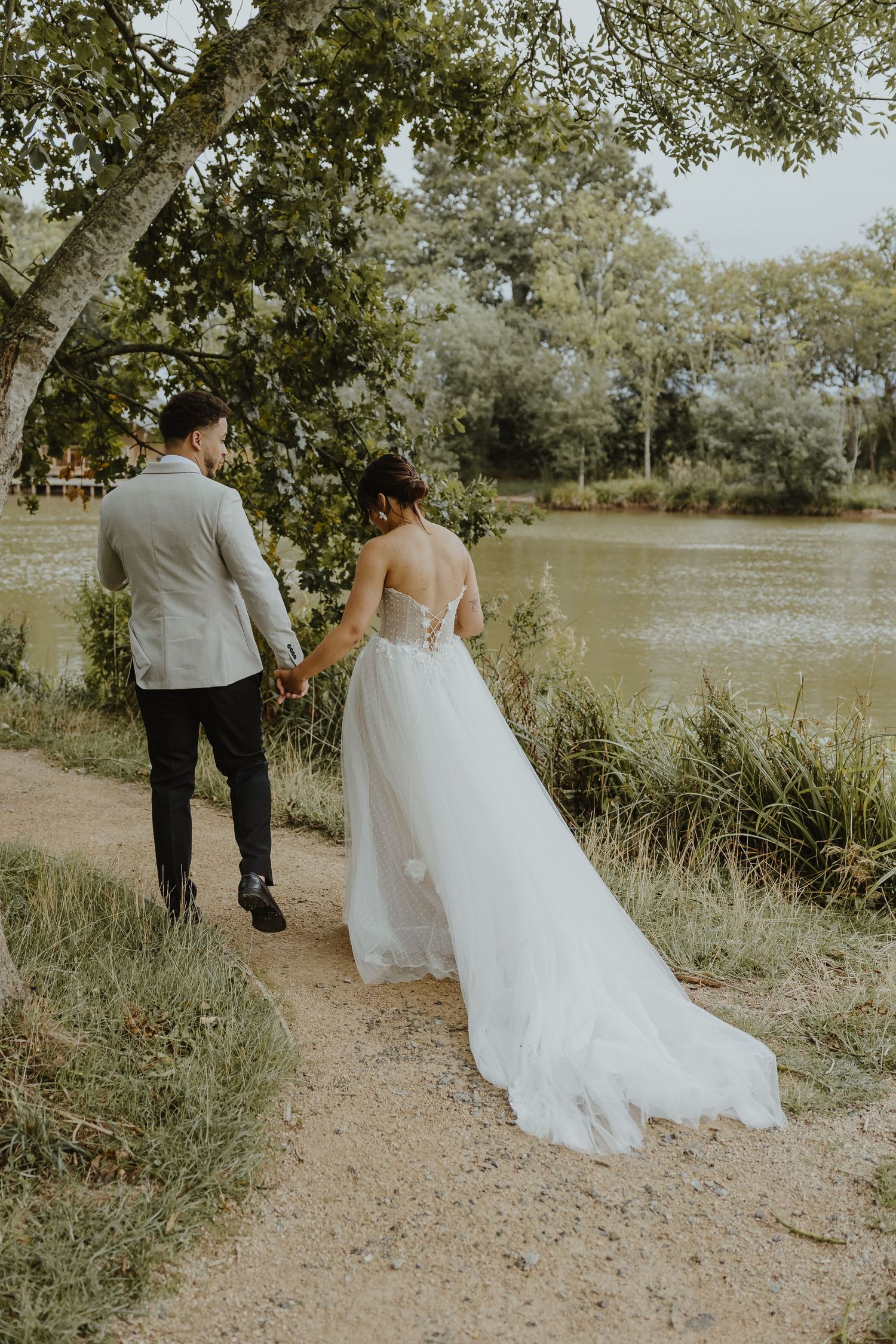 Wedding couple walking hand in hand along lakeside path.