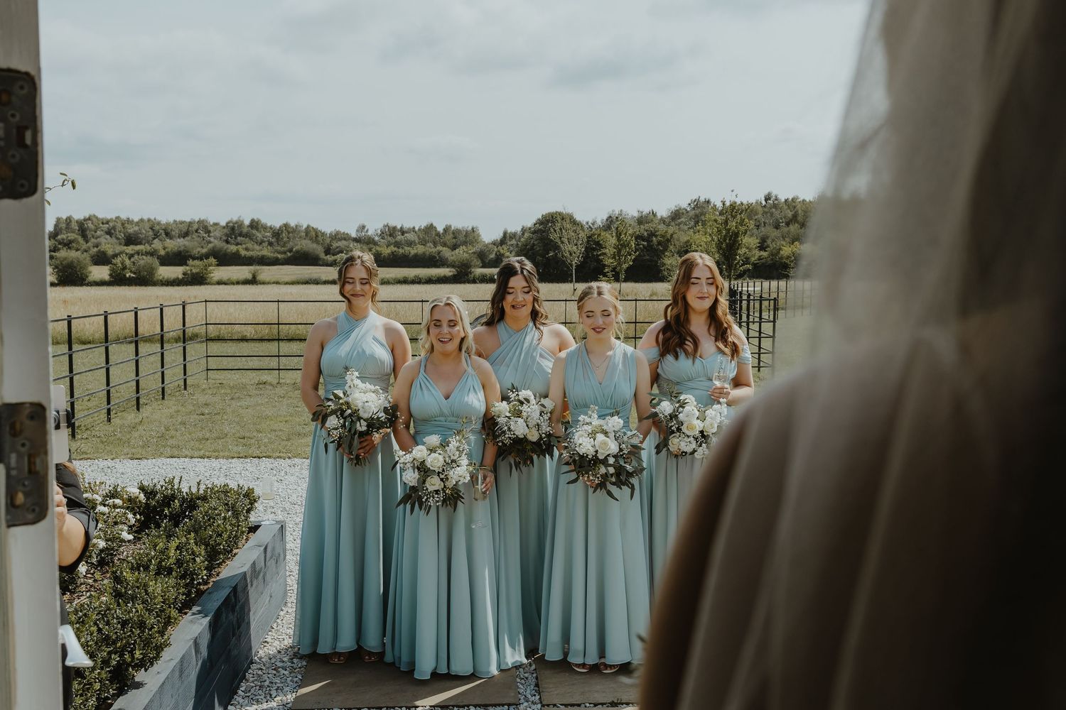 Bridesmaids in light blue dresses stand together at an outdoor wedding ceremony.