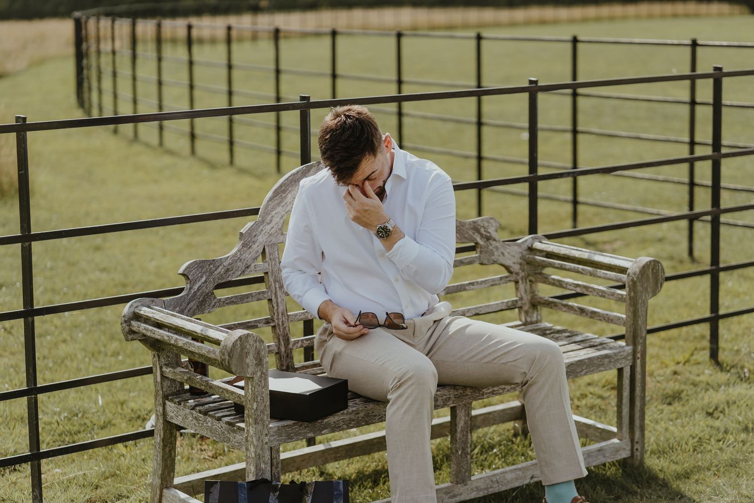 Person in formal attire reading papers while seated on wooden bleachers in a grassy field.