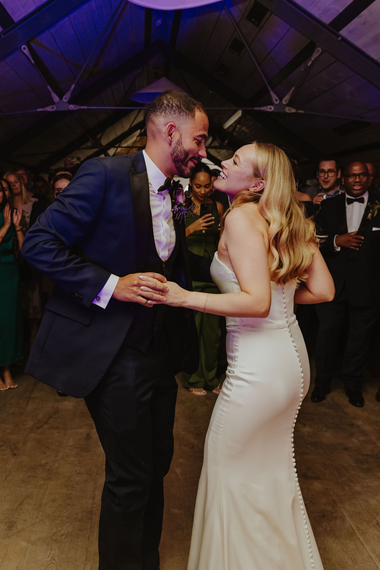 A couple shares a joyful dance moment at their wedding reception under purple lighting.