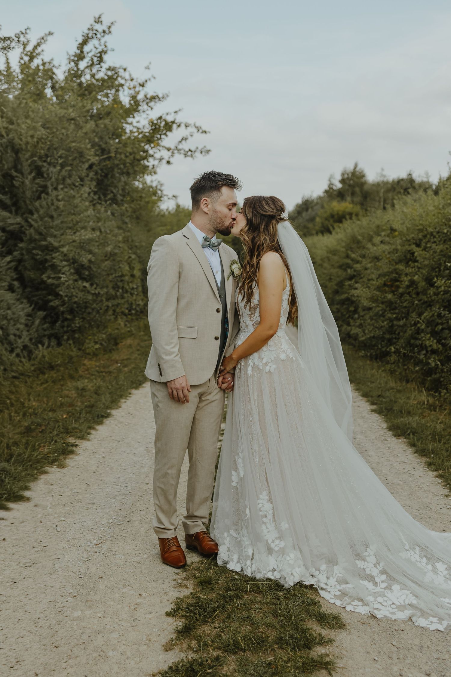 A romantic wedding portrait on a gravel path with lush greenery background.