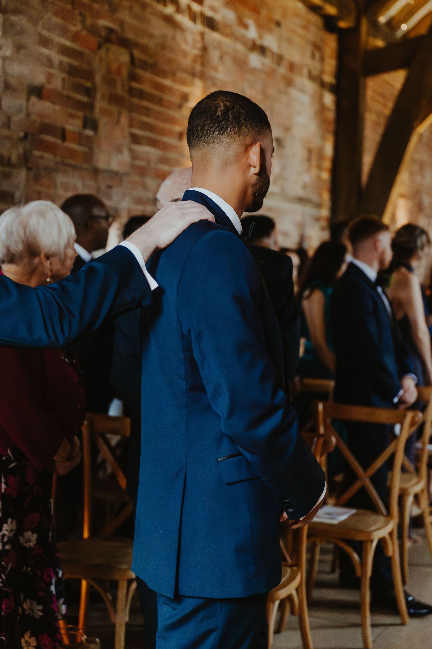 Wedding guests seated in rows at a rustic brick venue with wooden chairs.