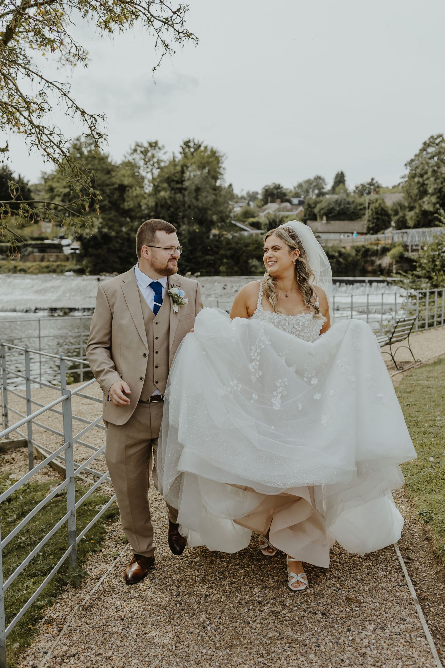 Bride and groom share playful moment on rustic fence during countryside photoshoot.