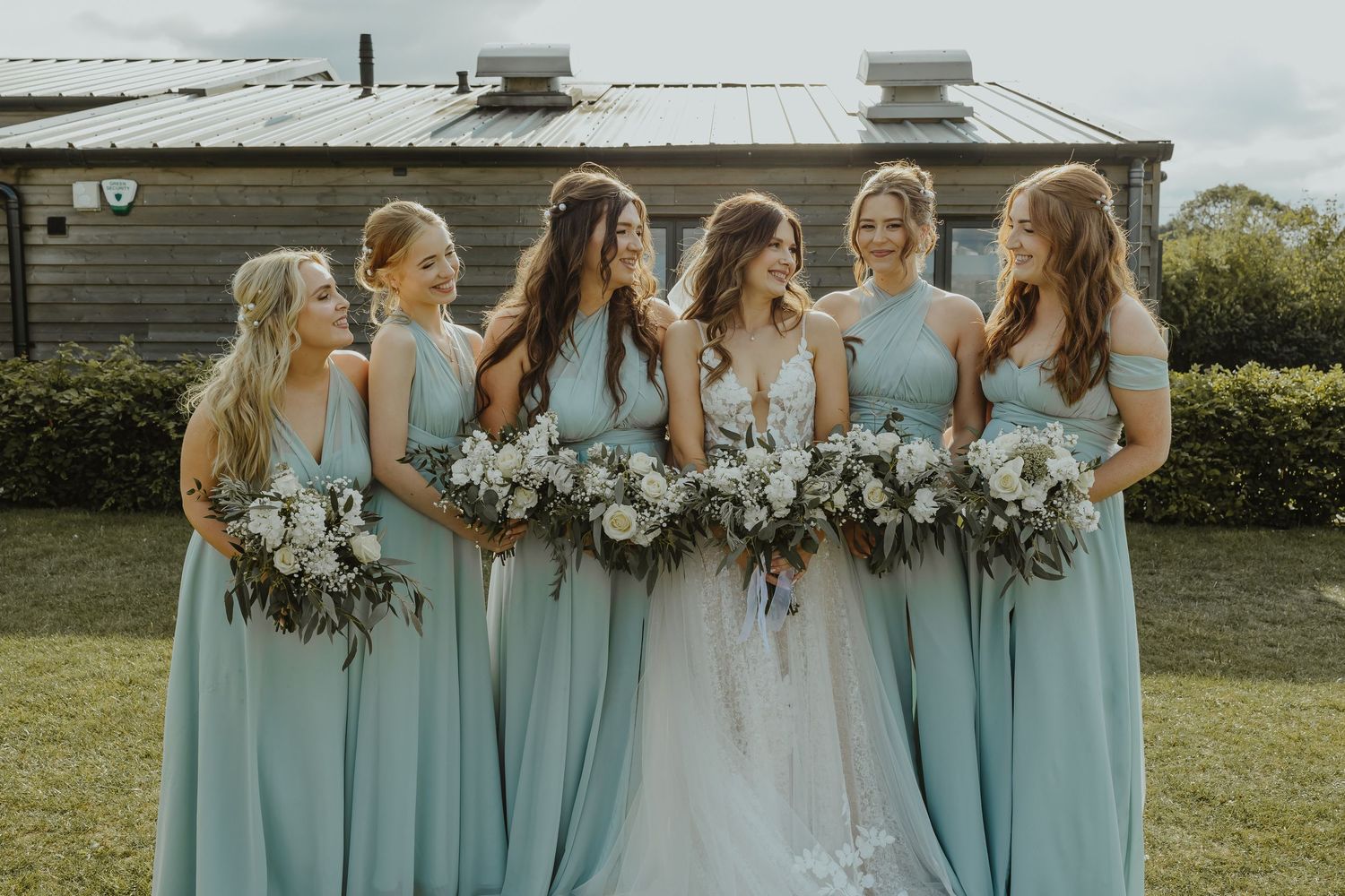 Wedding party with bridesmaids in blue dresses and bride in white lace gown holding bouquets.