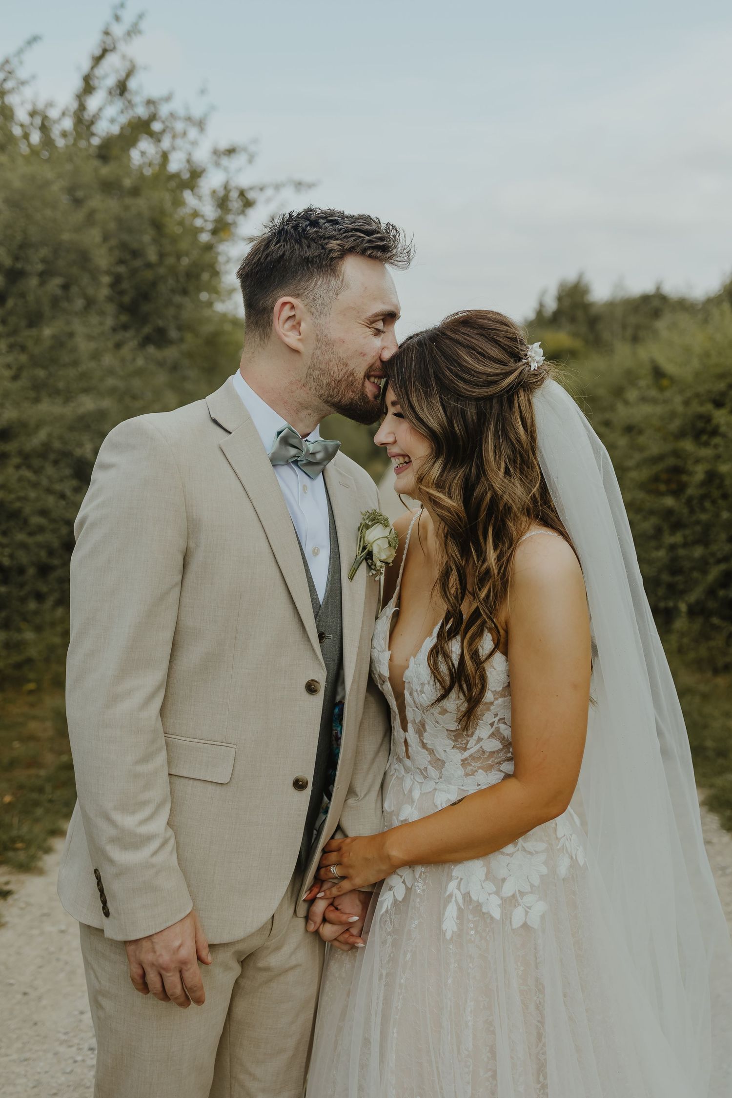 A tender moment between newlyweds on a countryside path in elegant wedding attire.