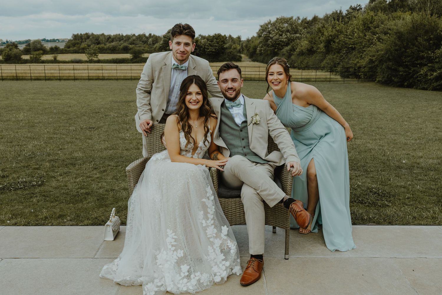 Wedding party poses on grassy field under cloudy sky.