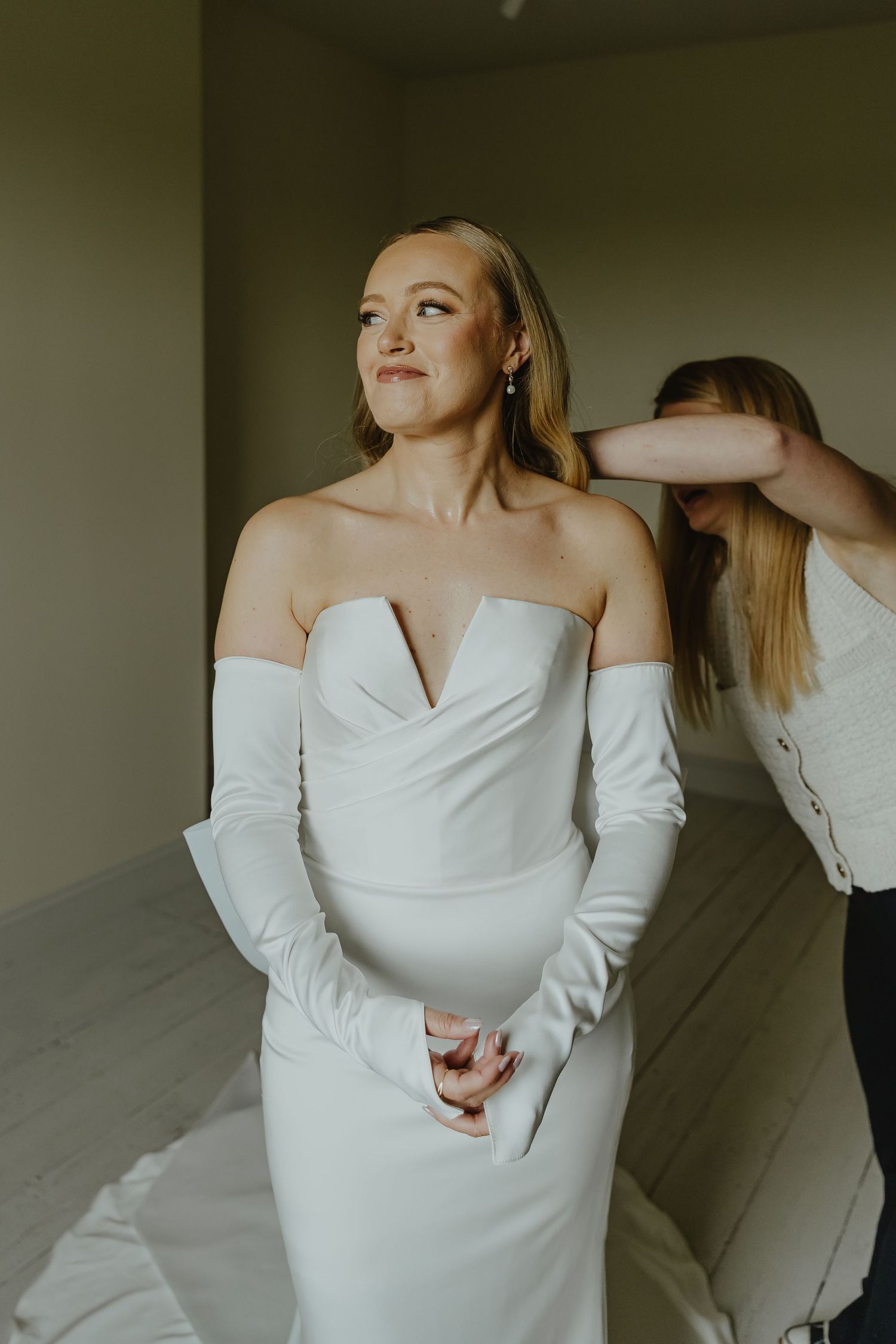 Elegant bride in form-fitting white dress with sweetheart neckline getting ready.
