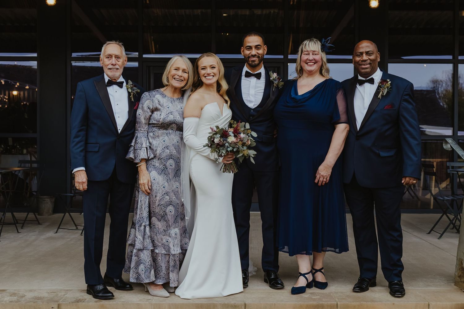 Wedding party and guests gather for group photo in elegant rustic venue.