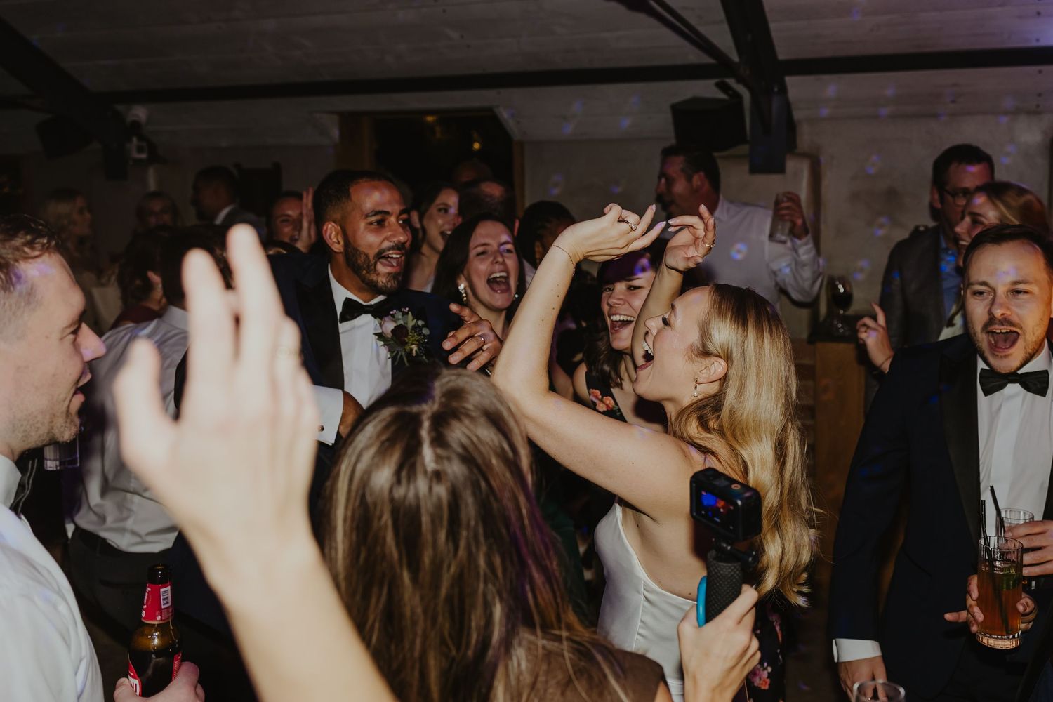Lively wedding reception dance party with guests celebrating in a dimly lit venue.
