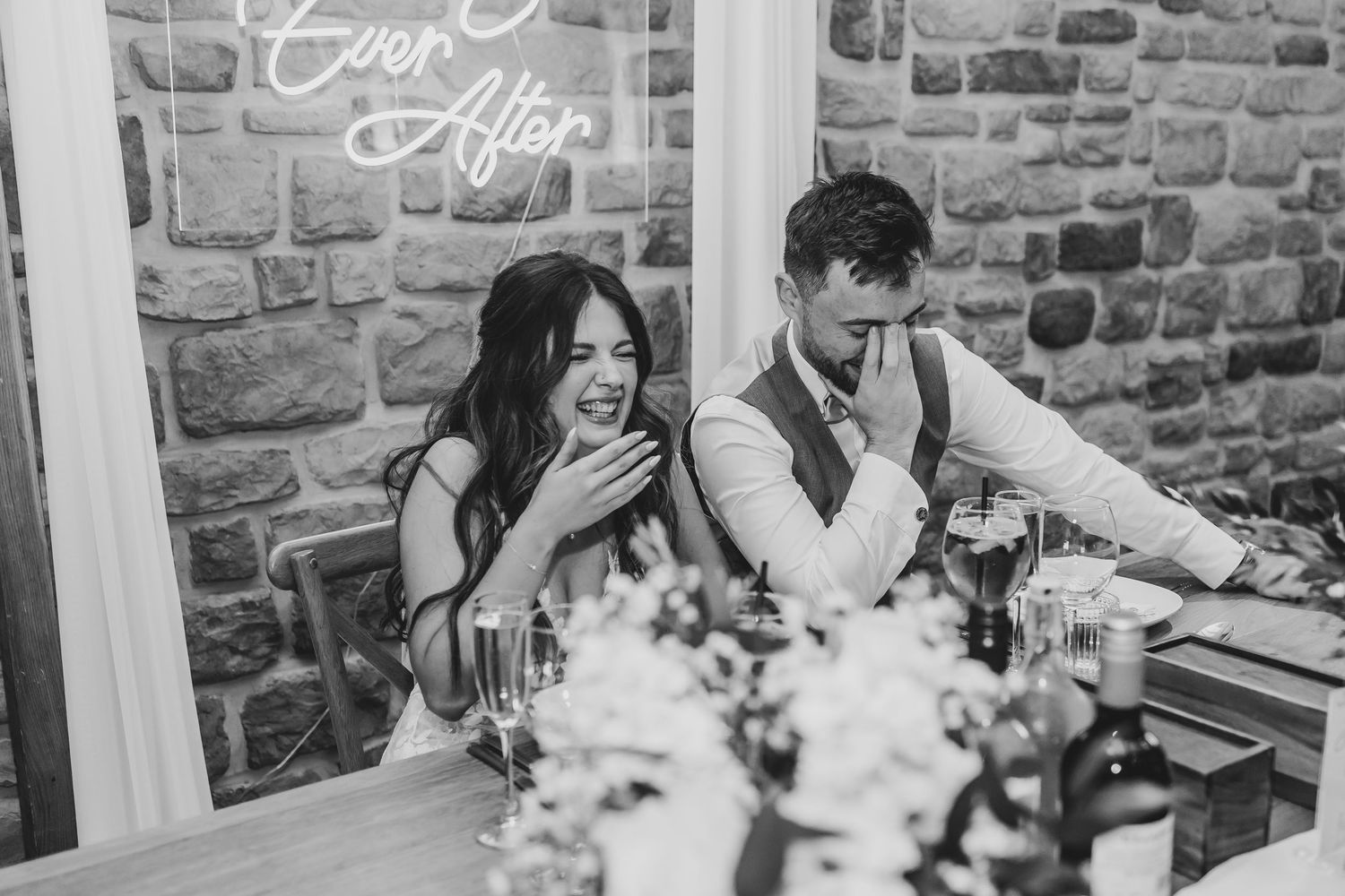 Wedding reception table setting against stone walls with white neon signage.