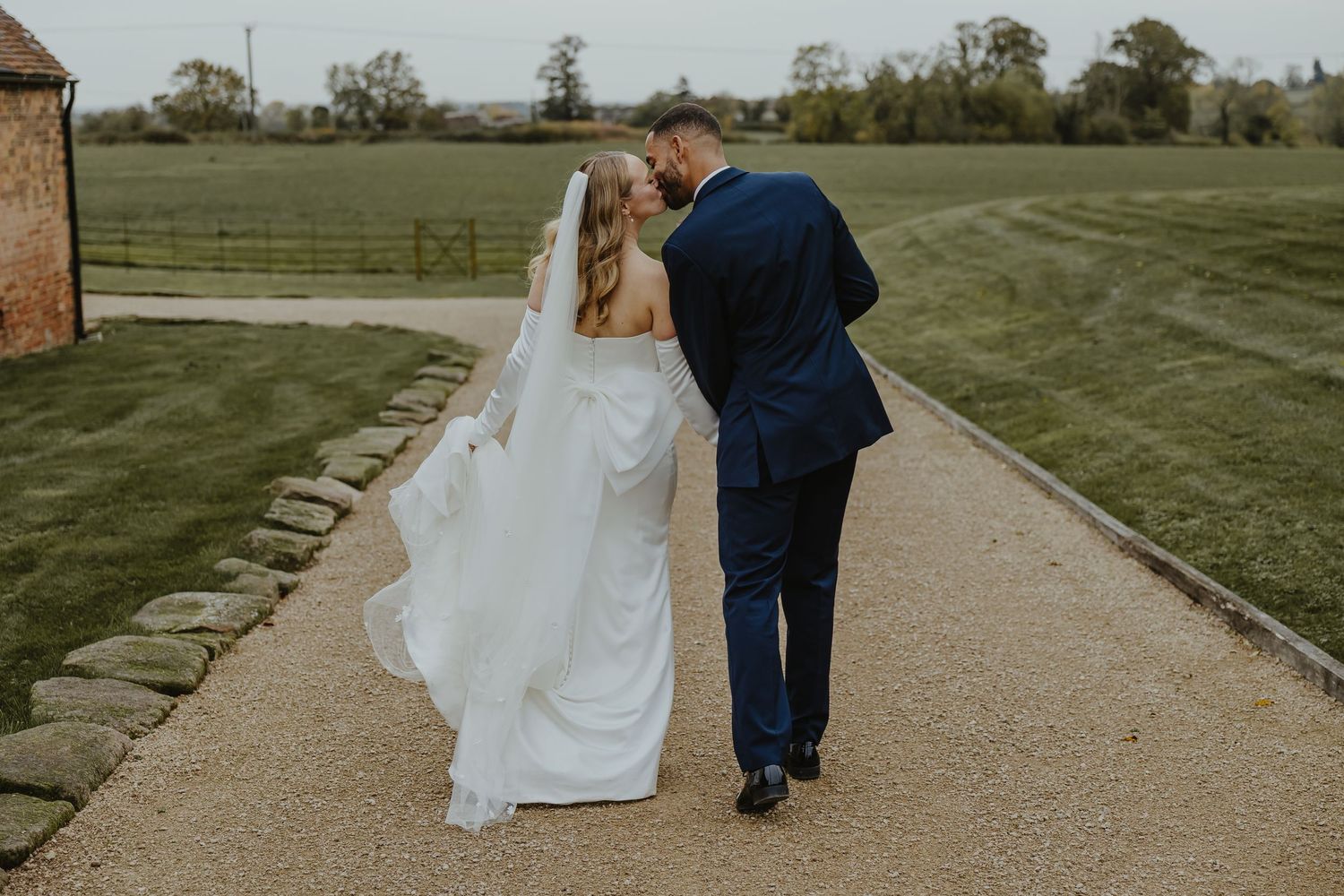 Couple walks along garden path with green landscape in background.