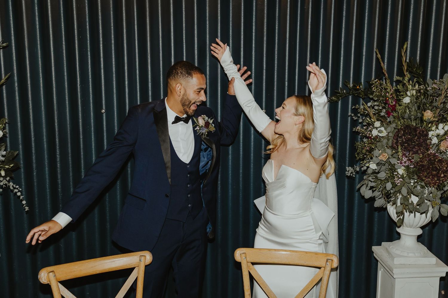 Celebratory dance moments at wedding reception with dark striped wall backdrop.