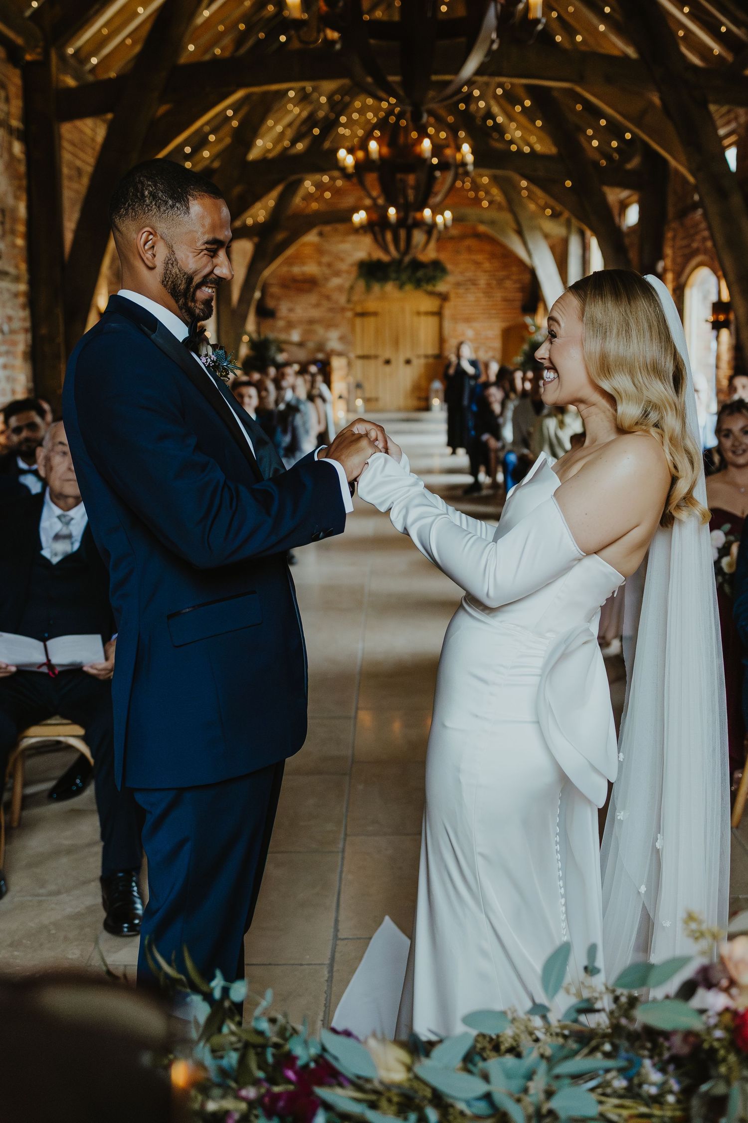 A couple exchanges rings during their wedding ceremony in a rustic venue with exposed beams.