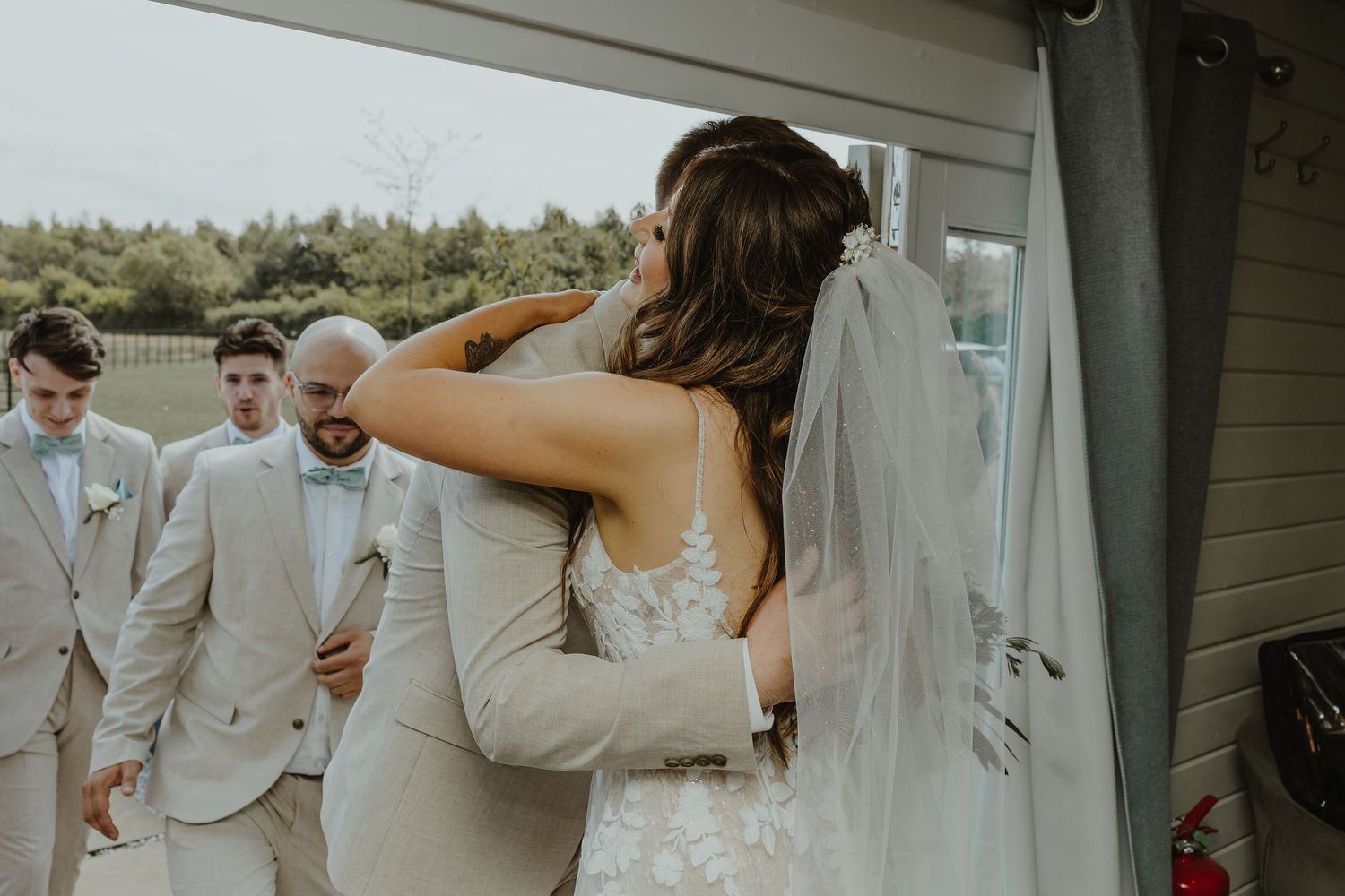 Groomsmen in light tan suits stand together at an outdoor wedding.