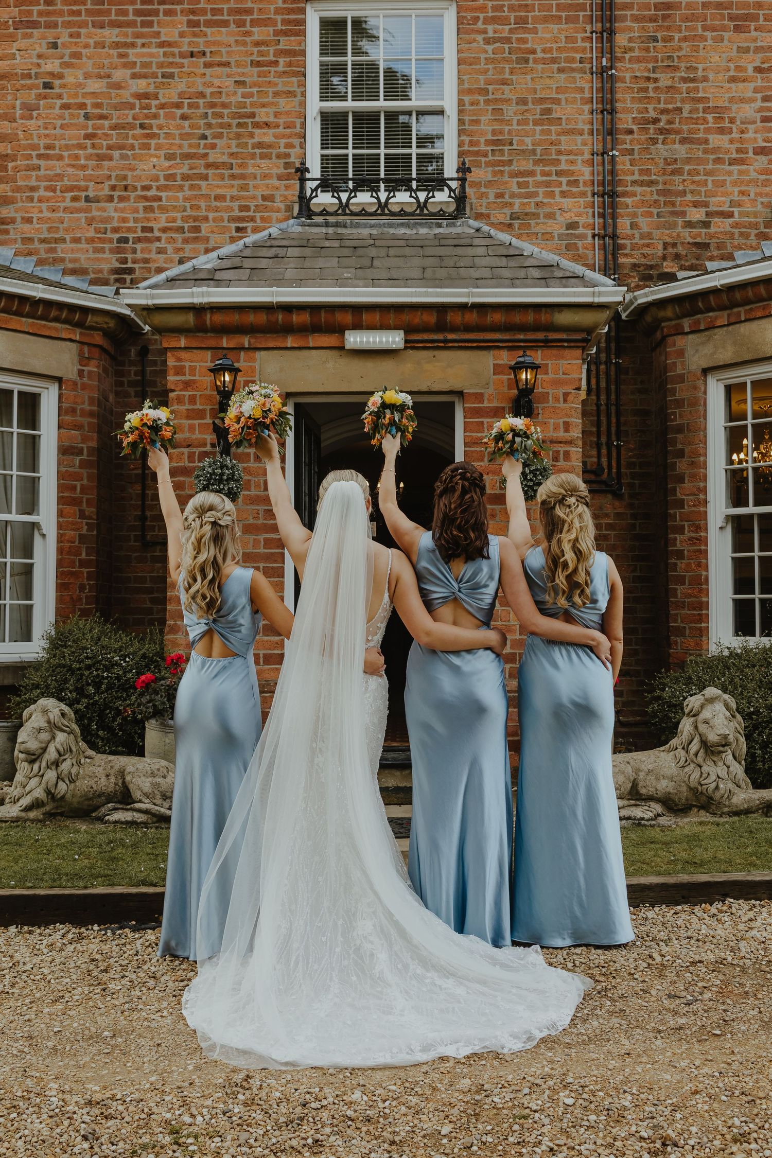 Bridesmaids in light blue dresses helping with wedding dress train.
