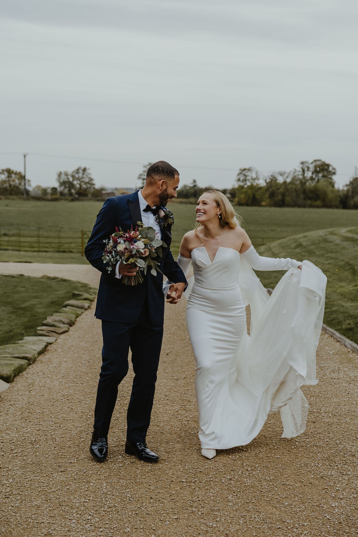 Happy couple walking and laughing together on a gravel path during their wedding.