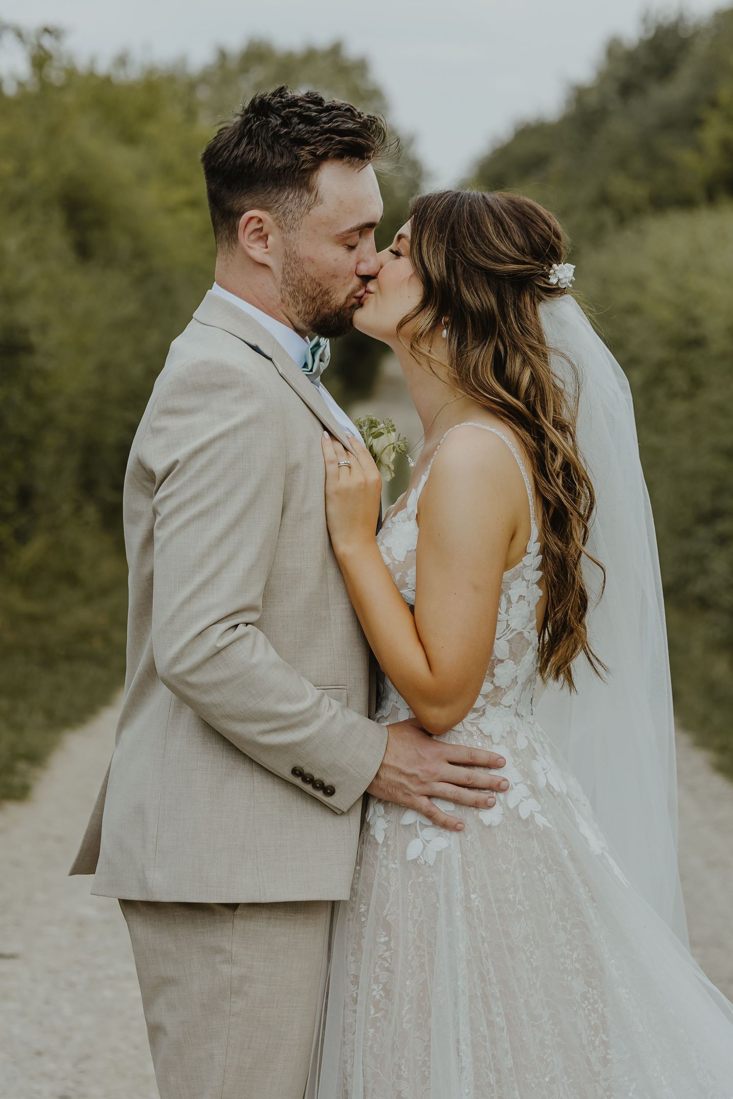 A tender wedding moment captured on a countryside path with the couple sharing a kiss.