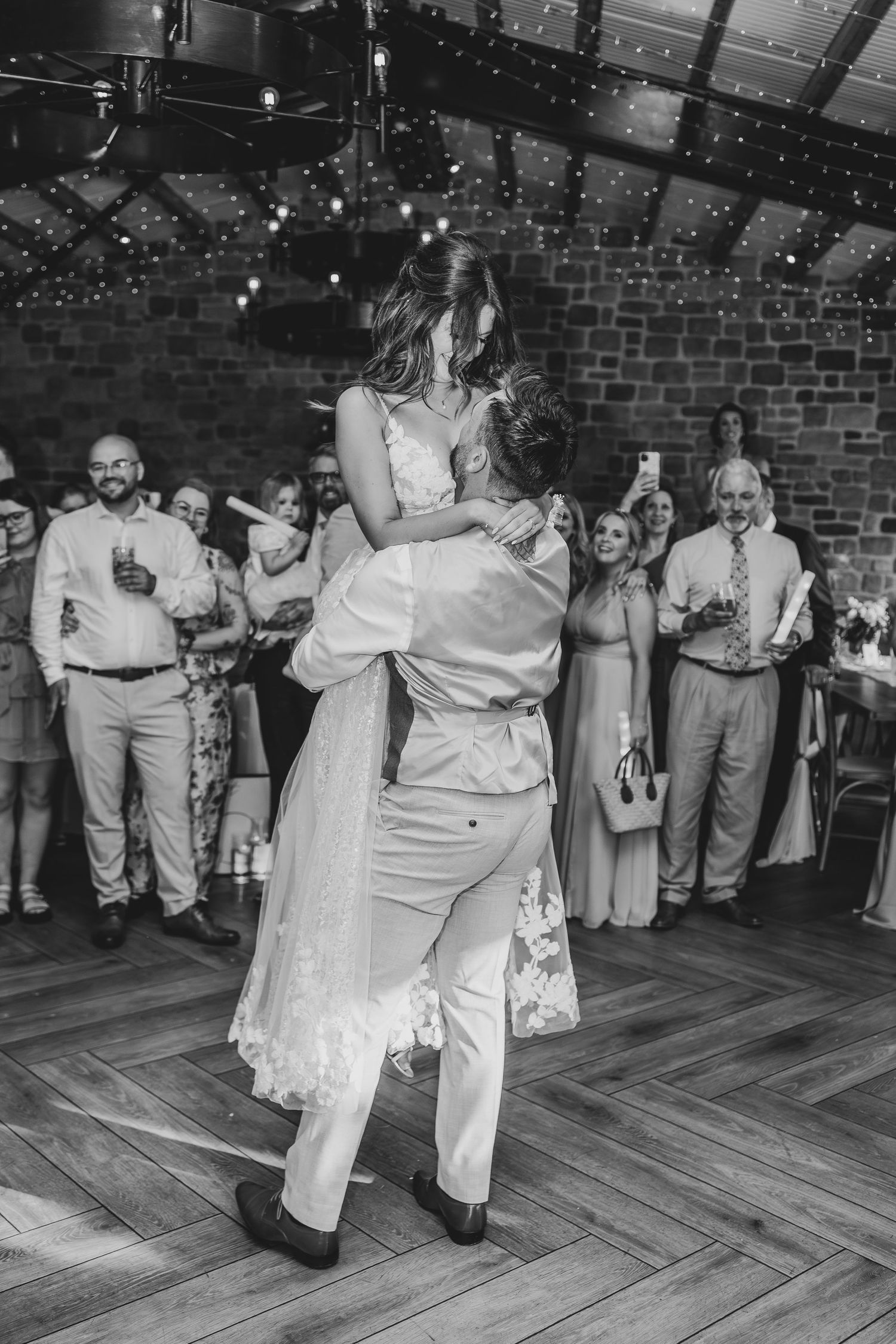 Black and white photo of a romantic first dance lift in a rustic reception venue.
