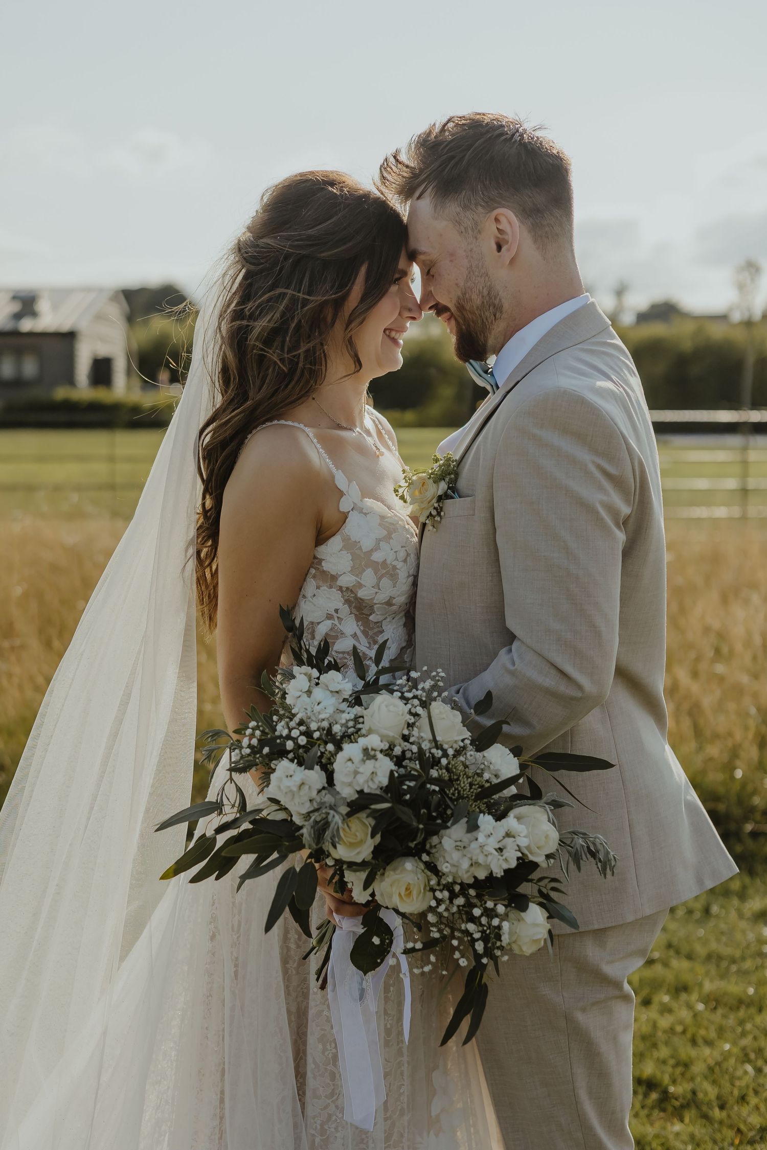 Romantic close-up of couple with white floral bouquet in countryside setting.