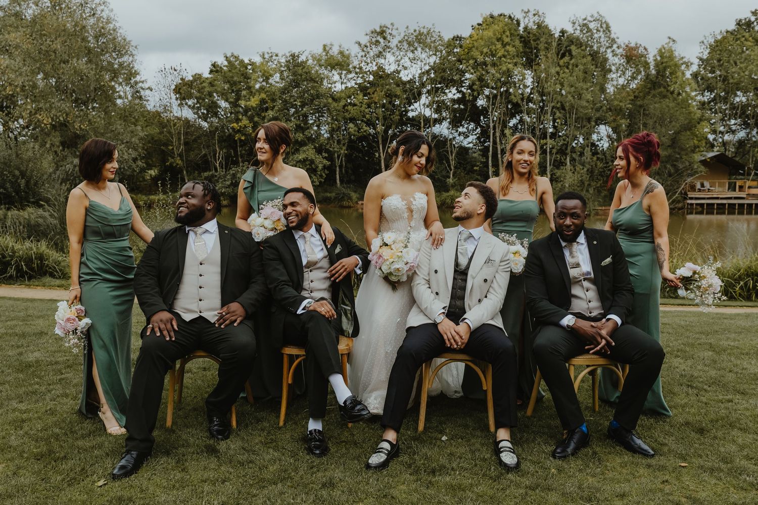 Wedding party group photo with bridesmaids in green dresses and groomsmen in formal attire.