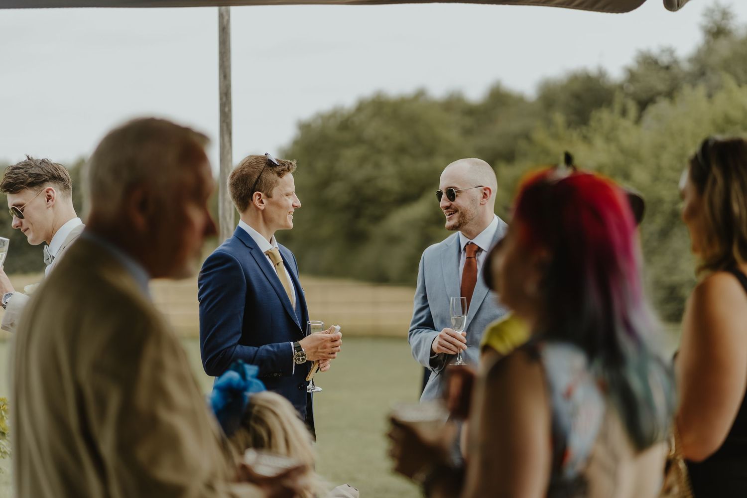 Wedding guests gather outdoors under cloudy sky during ceremony.