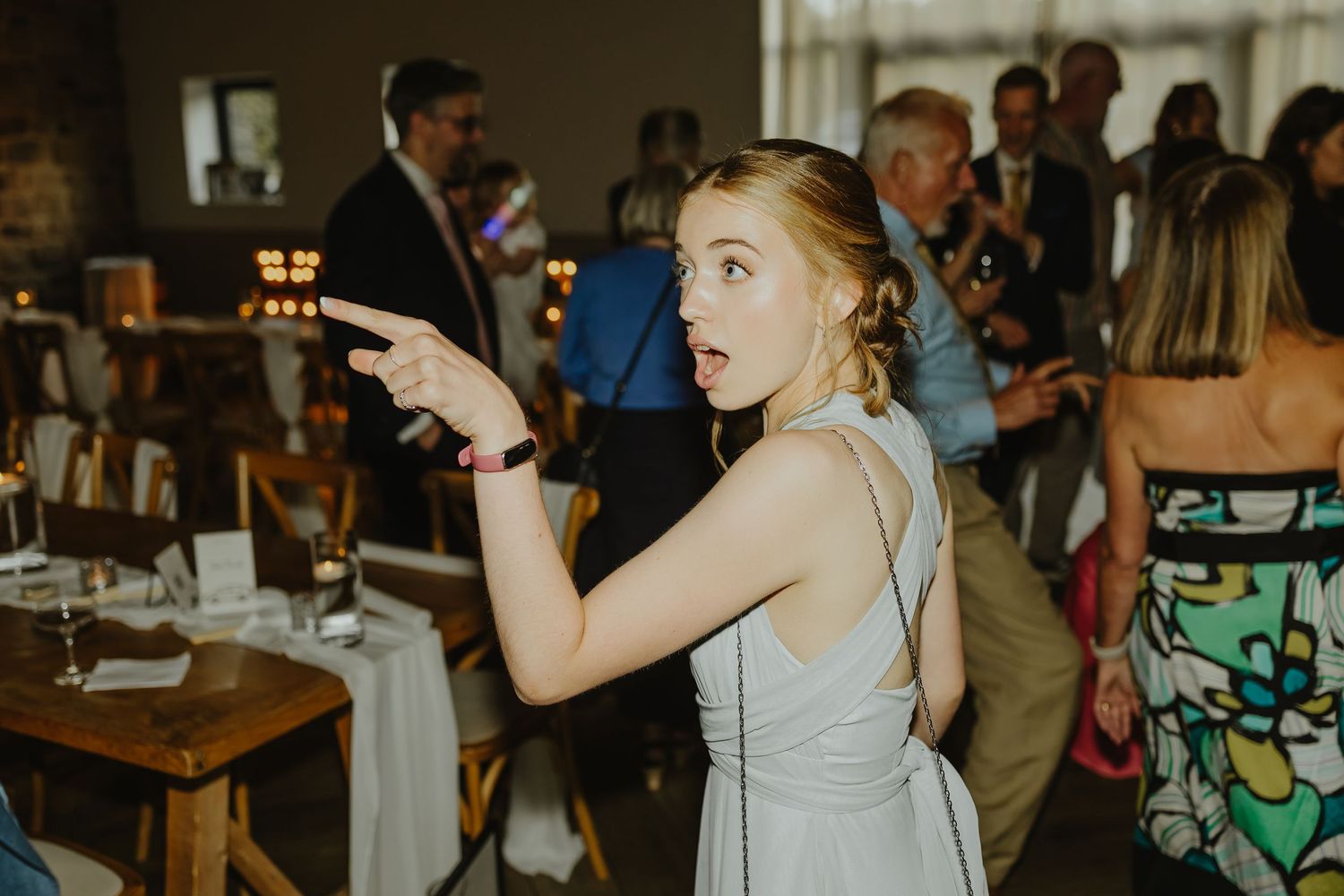 Wedding guests dancing energetically in a dimly lit reception venue with brick walls.