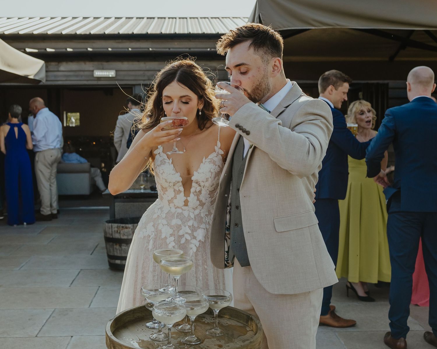 Newlyweds sharing a playful moment while drinking champagne at their outdoor wedding reception.