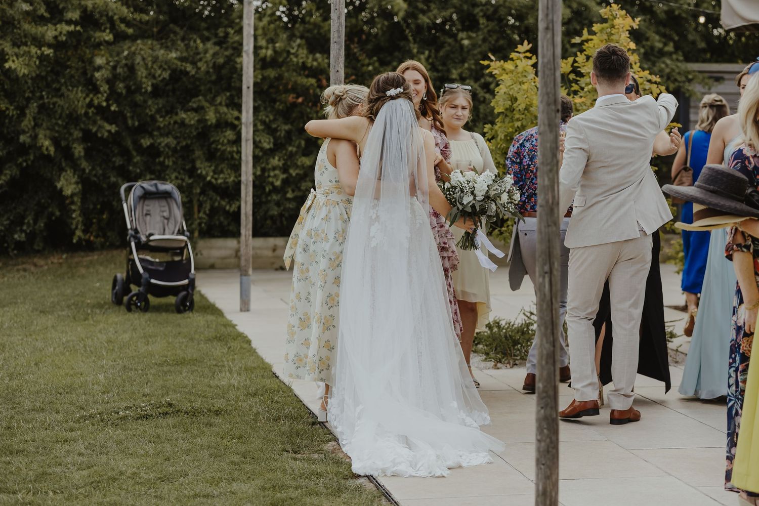 Wedding ceremony guests gather outdoors under trees at a rustic venue.