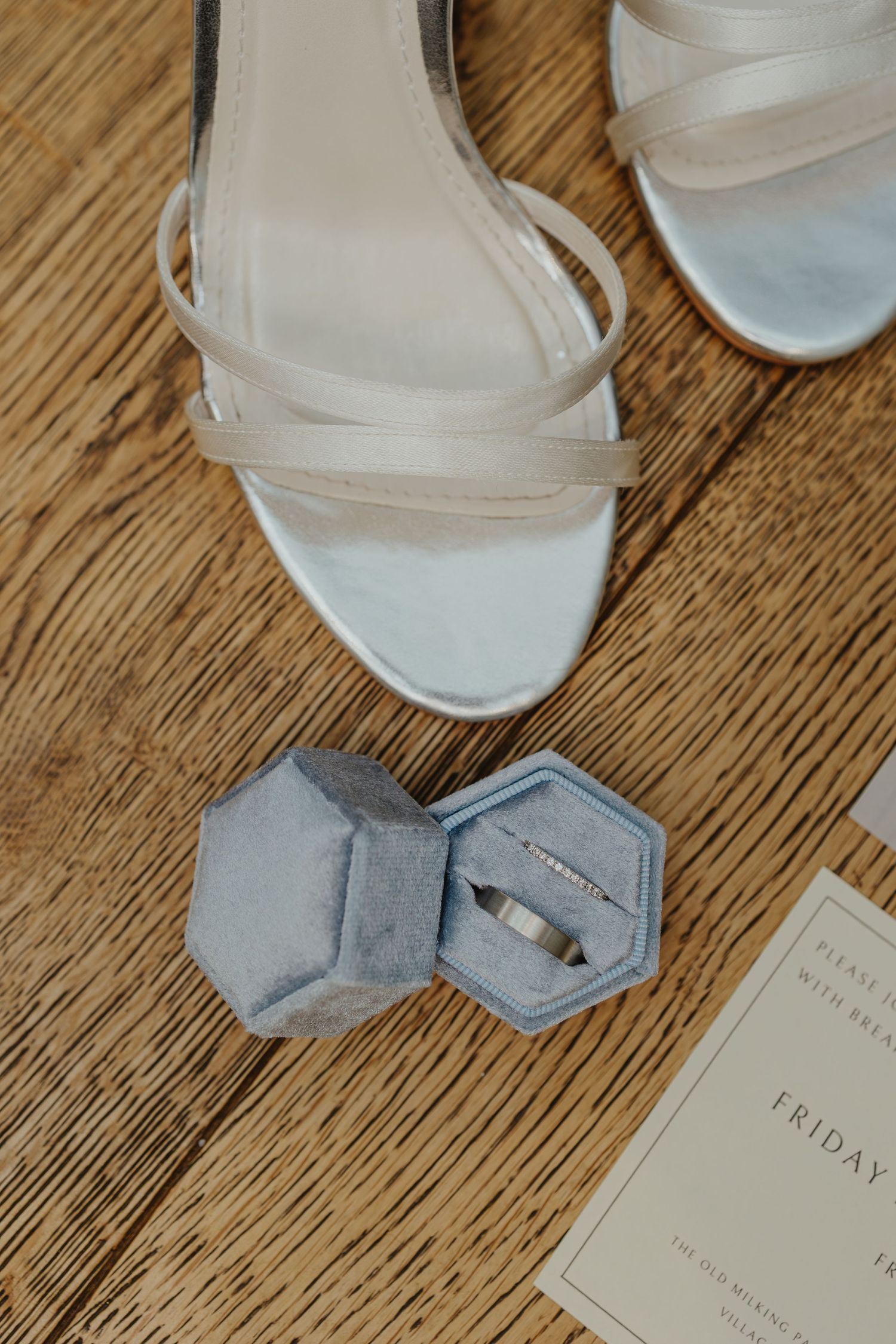 White bridal shoes and wedding stationery displayed on wooden flooring.