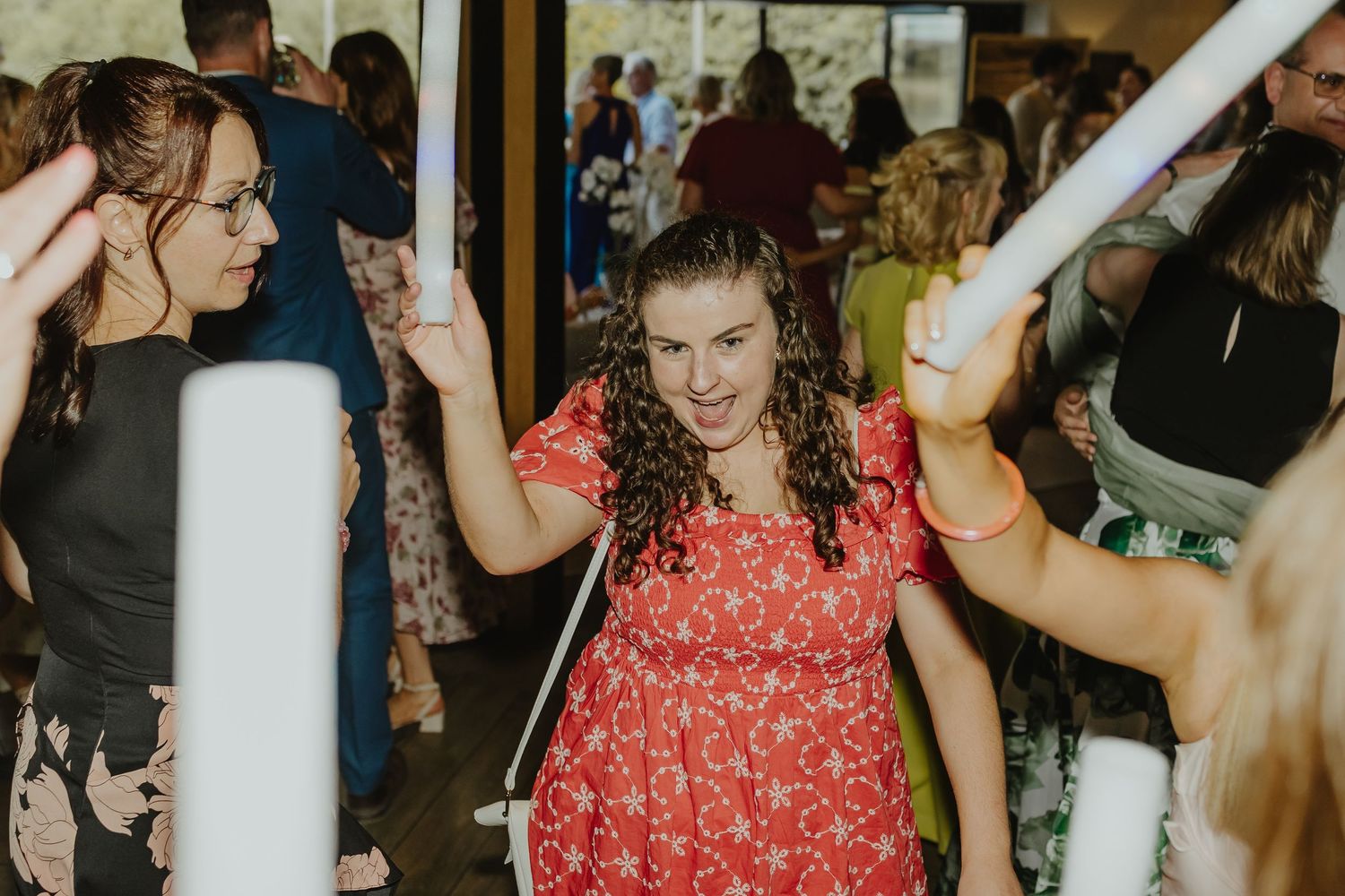 Wedding guests dancing and celebrating on a dance floor with a red dress visible in the crowd.