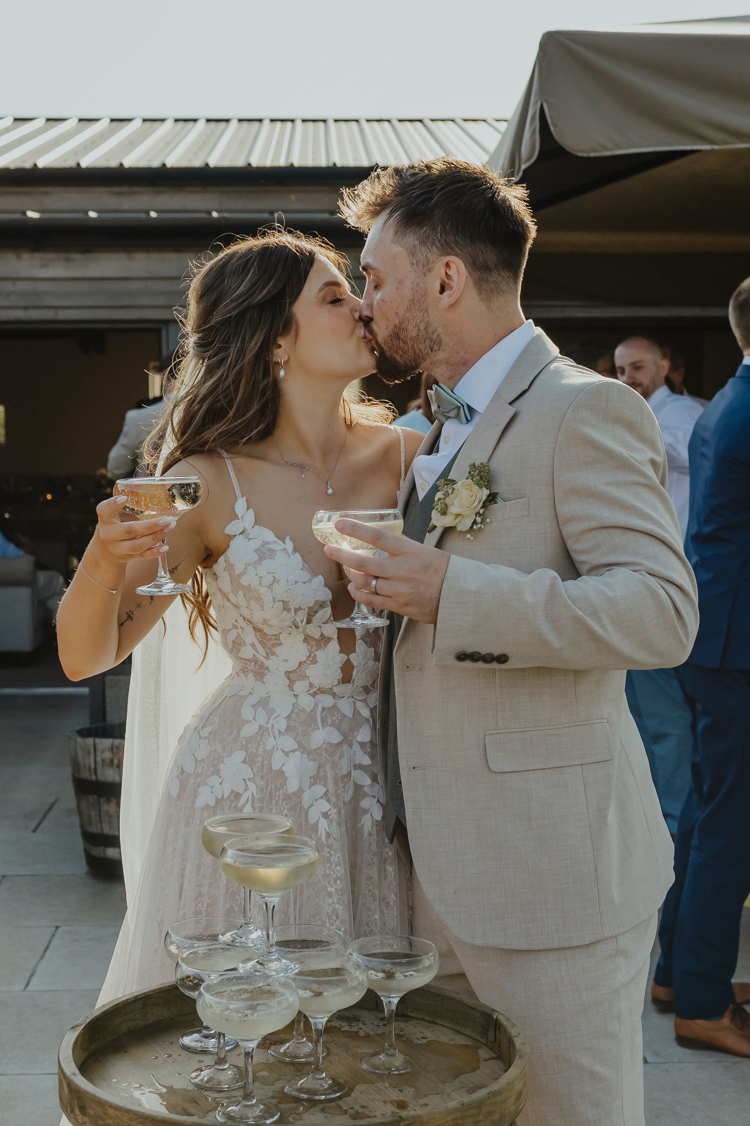 A romantic champagne toast between newlyweds in elegant wedding attire at an outdoor reception.