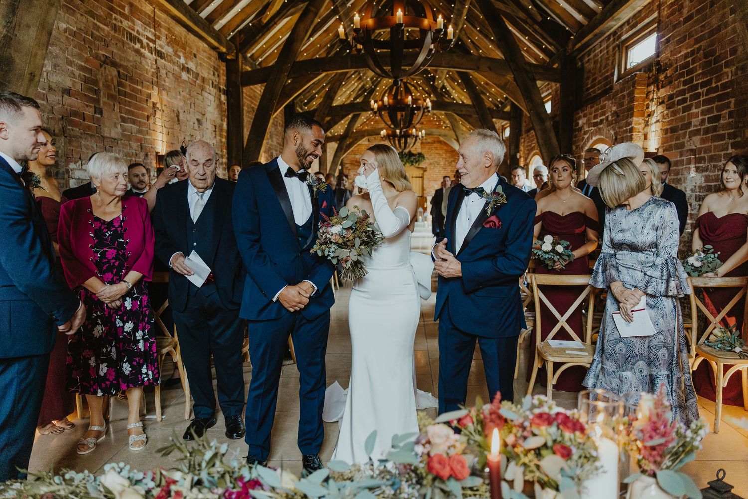 Wedding reception in a rustic brick barn with exposed wooden beams and decorative lighting.