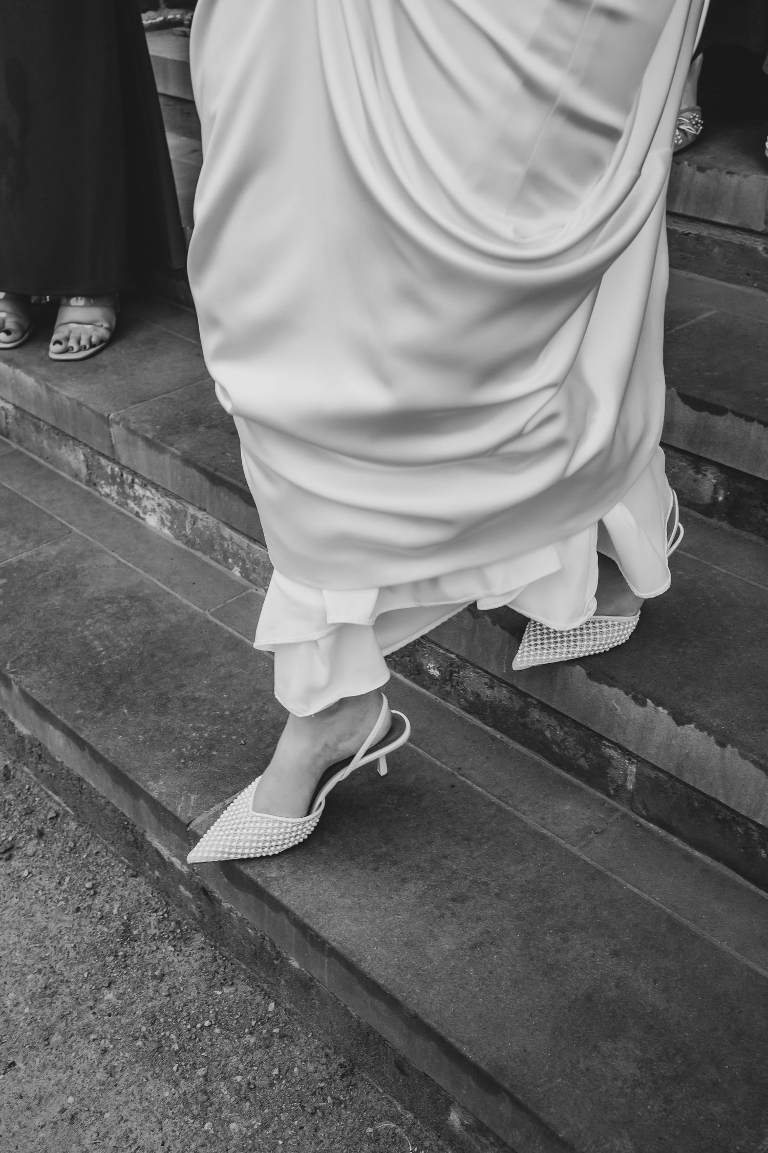 Close-up of bride's white dress and shoes on stone steps.