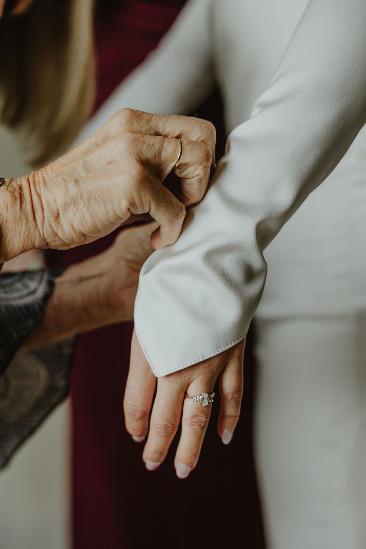 Close-up of hands showing an engagement ring and wedding band against a white dress sleeve.