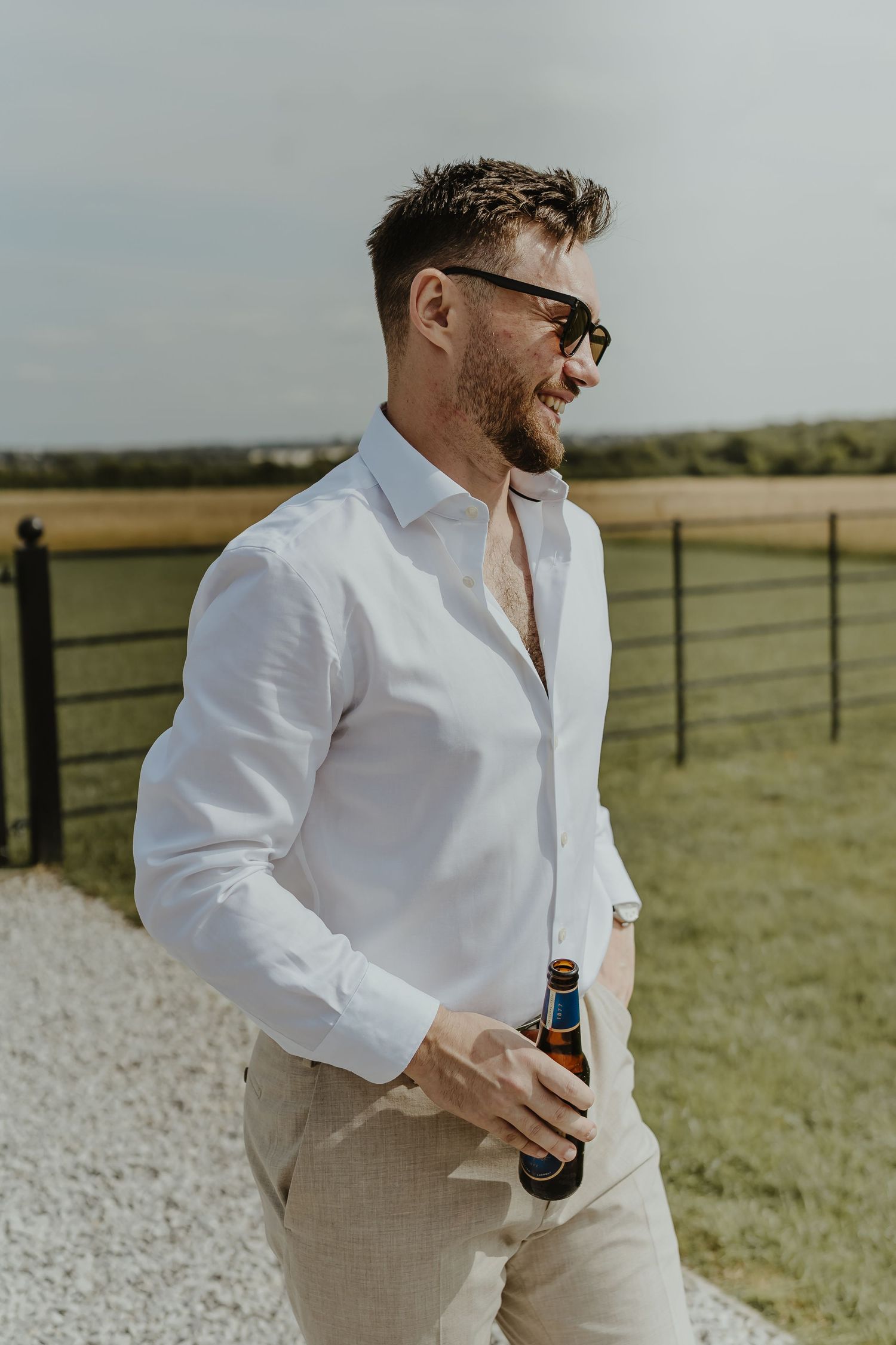 People in white shirts and khaki pants holding drinks outdoors against rural backdrop.