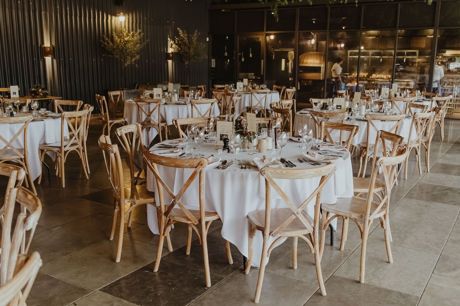 Modern wedding reception venue with white round tables and cross-back chairs.