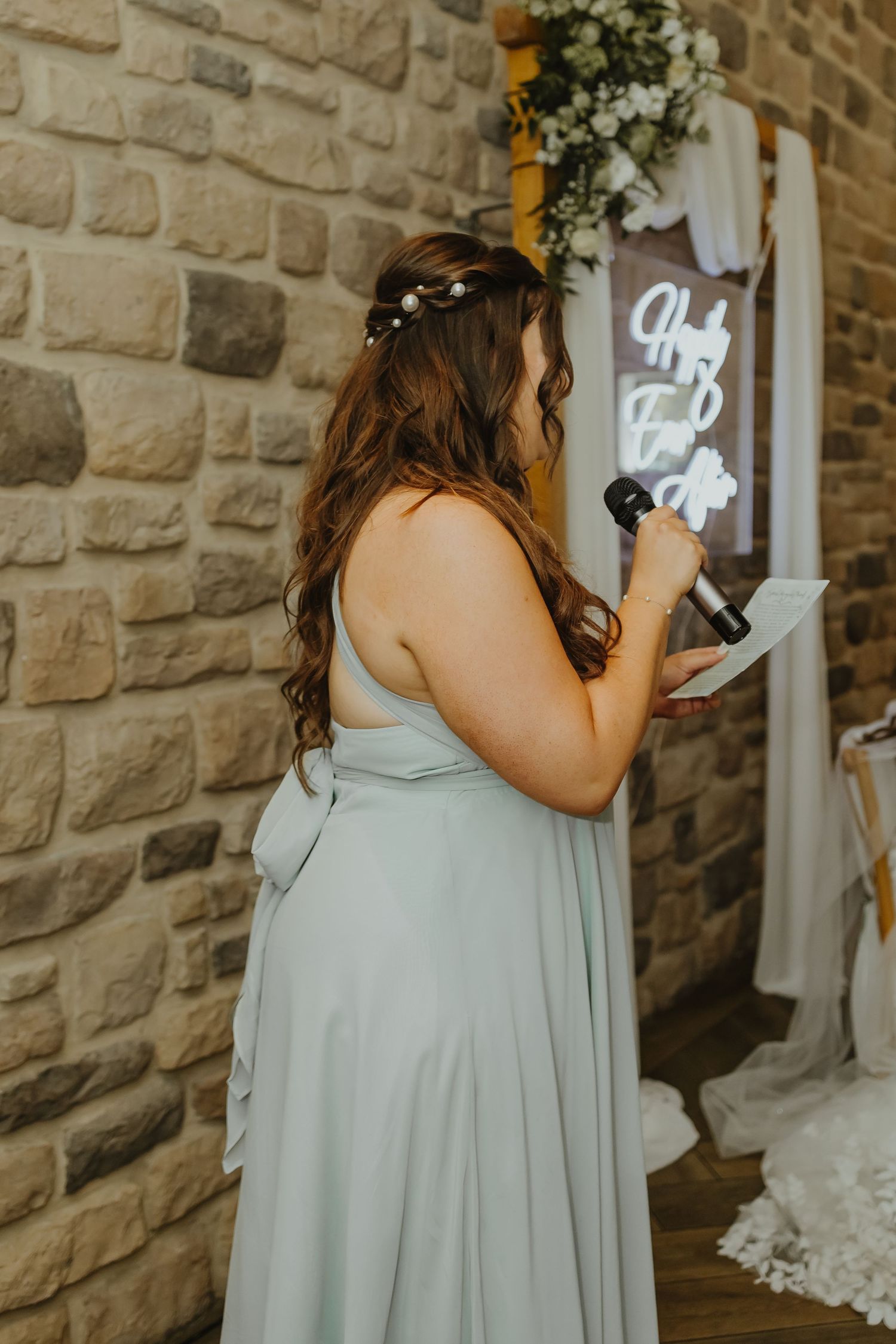 Bridesmaid in sage green dress at rustic stone venue.