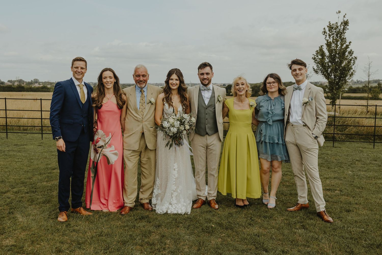 Wedding party members in coordinated formal attire pose together on a grassy field.