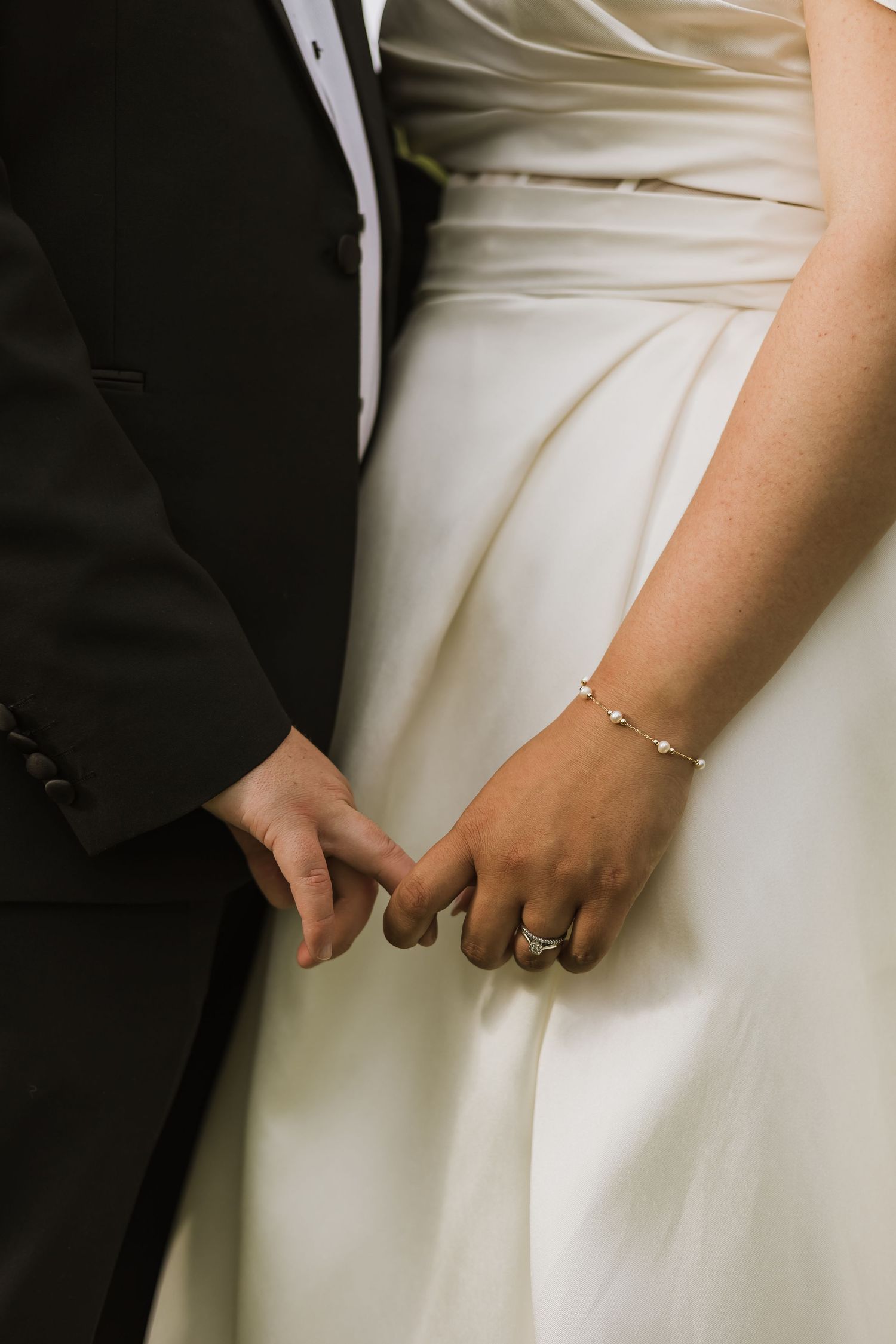 Bride and groom holding hands at wedding, bride wearing diamond ring and gold bracelet with white gown.