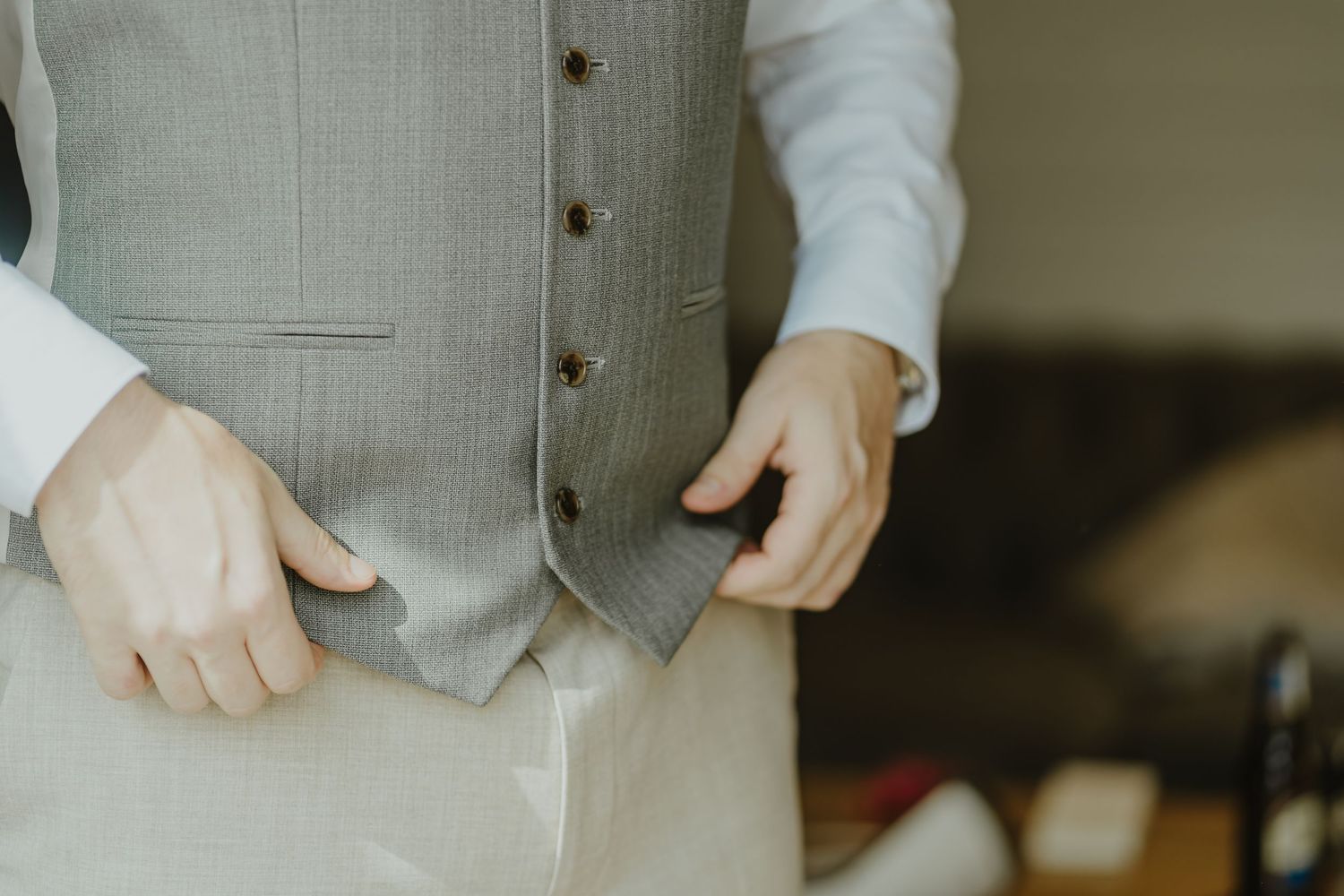 Close-up shot of hands adjusting a grey formal vest.