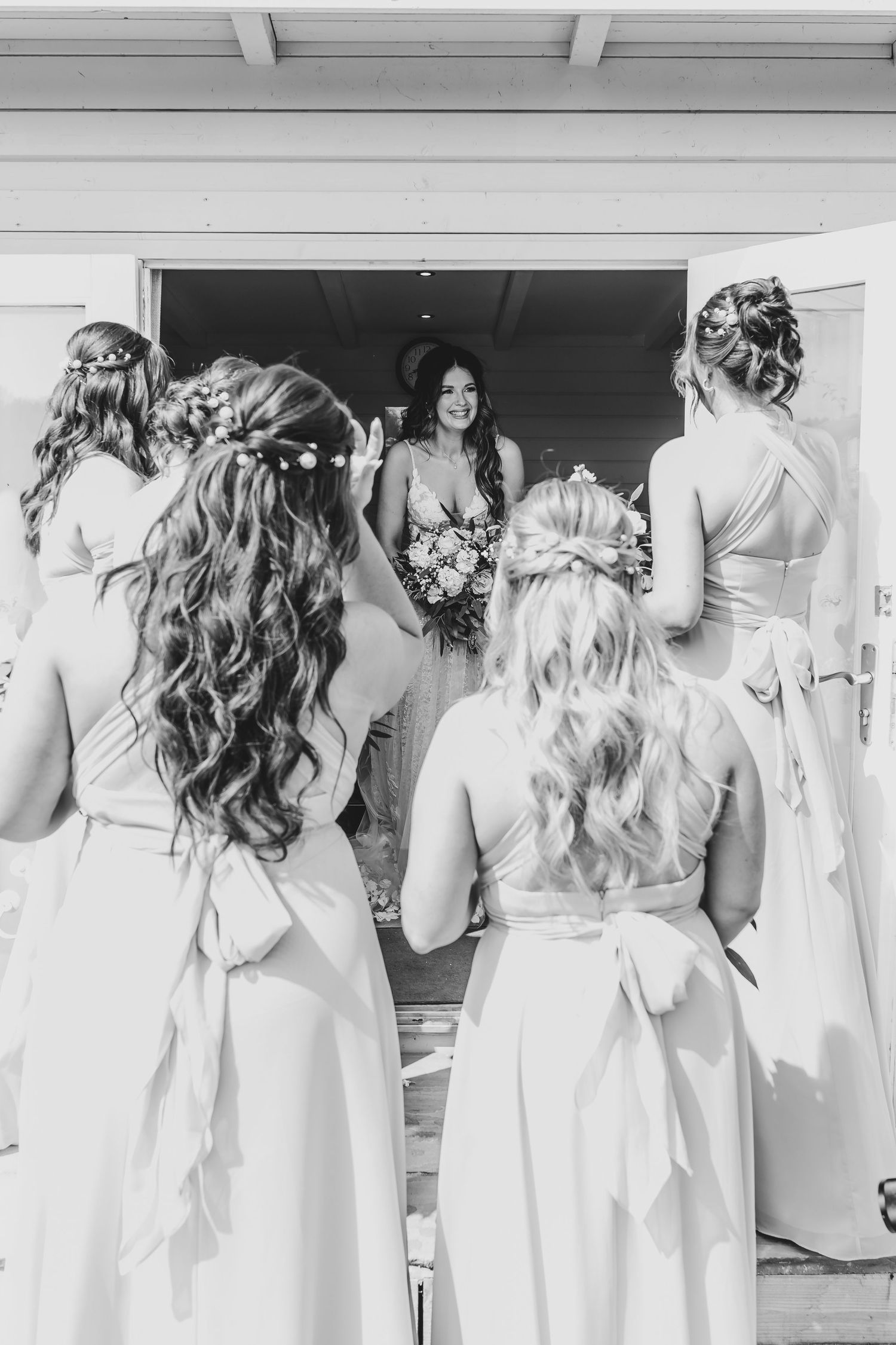A row of bridesmaids in white dresses shown from behind with styled curled hair.