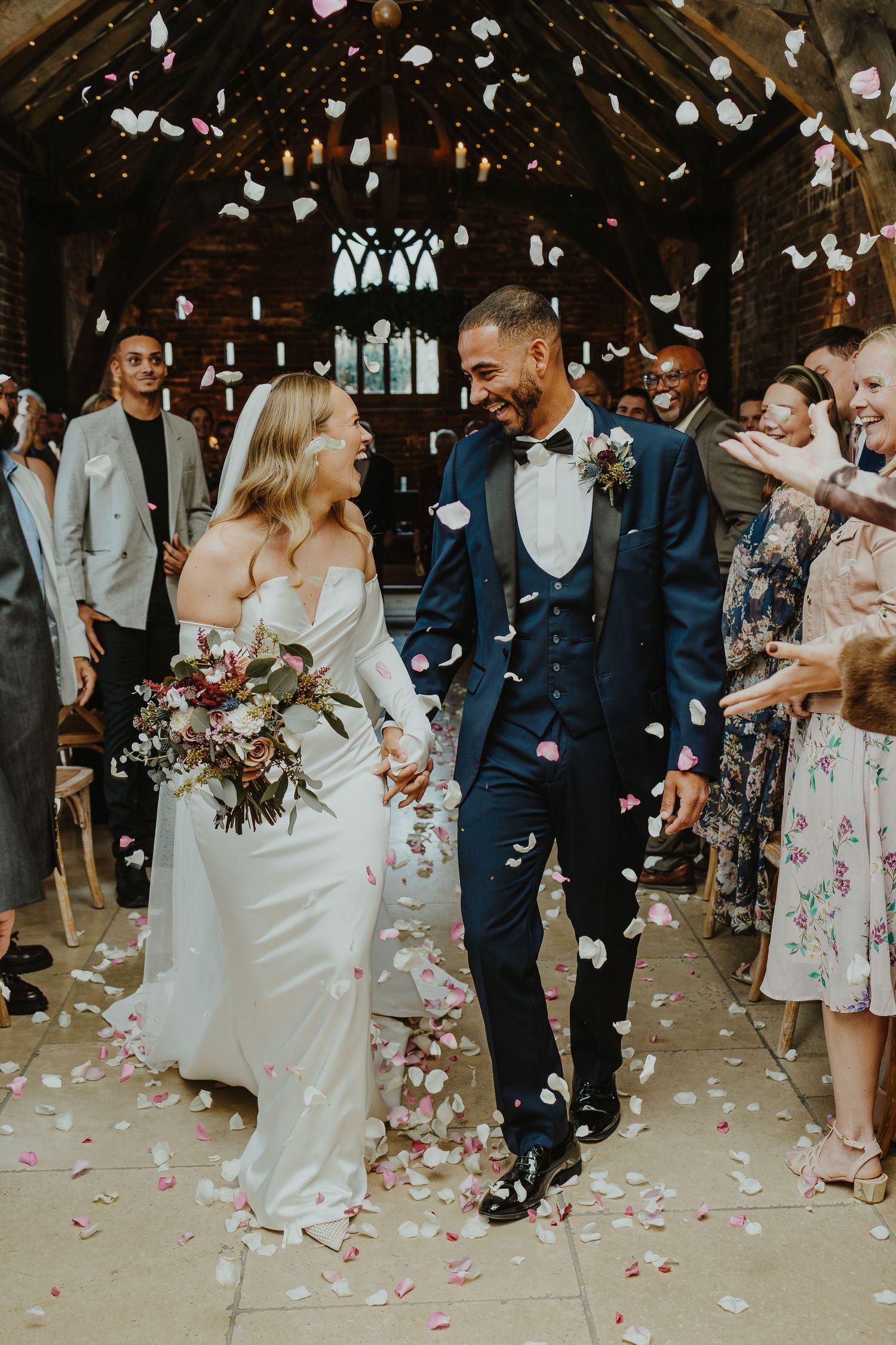Wedding party celebrates with flower petals being tossed in joyful corridor exit.