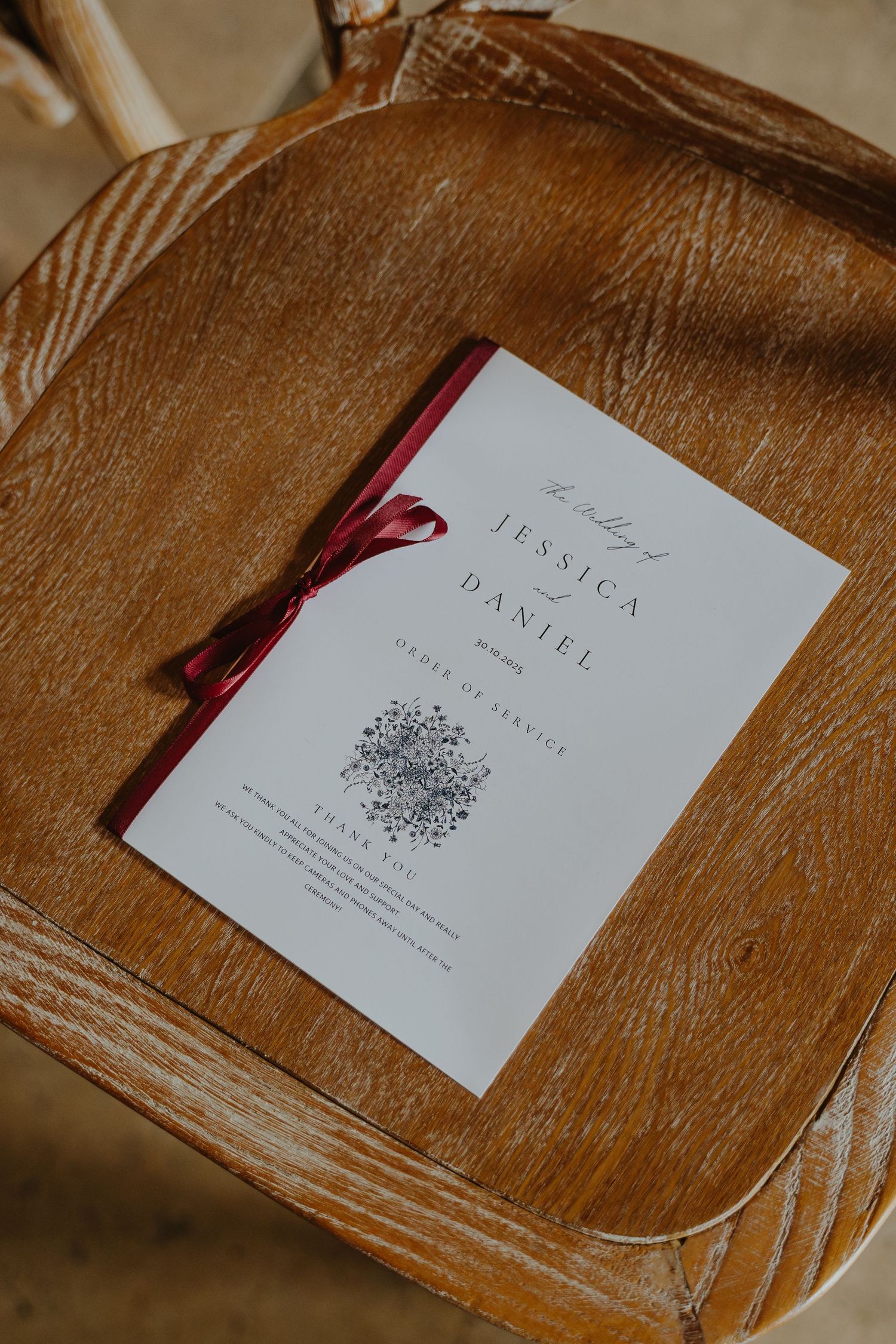 Wedding invitation with burgundy ribbon detail lying on rustic wooden surface.
