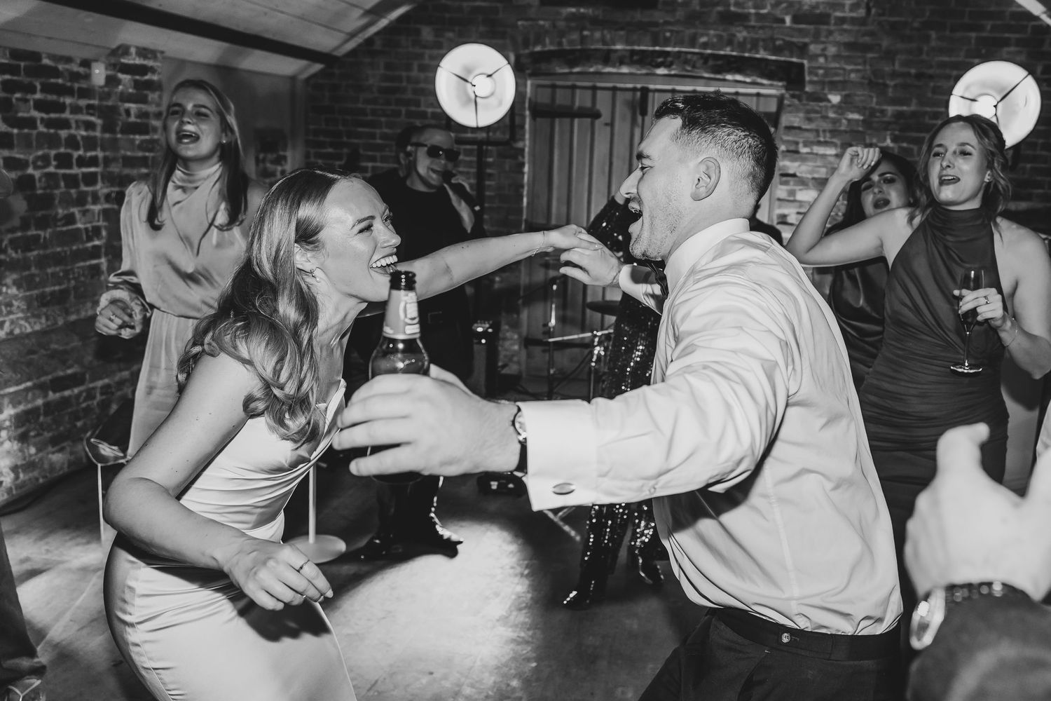 Wedding guests dancing and celebrating in a rustic brick-walled venue.