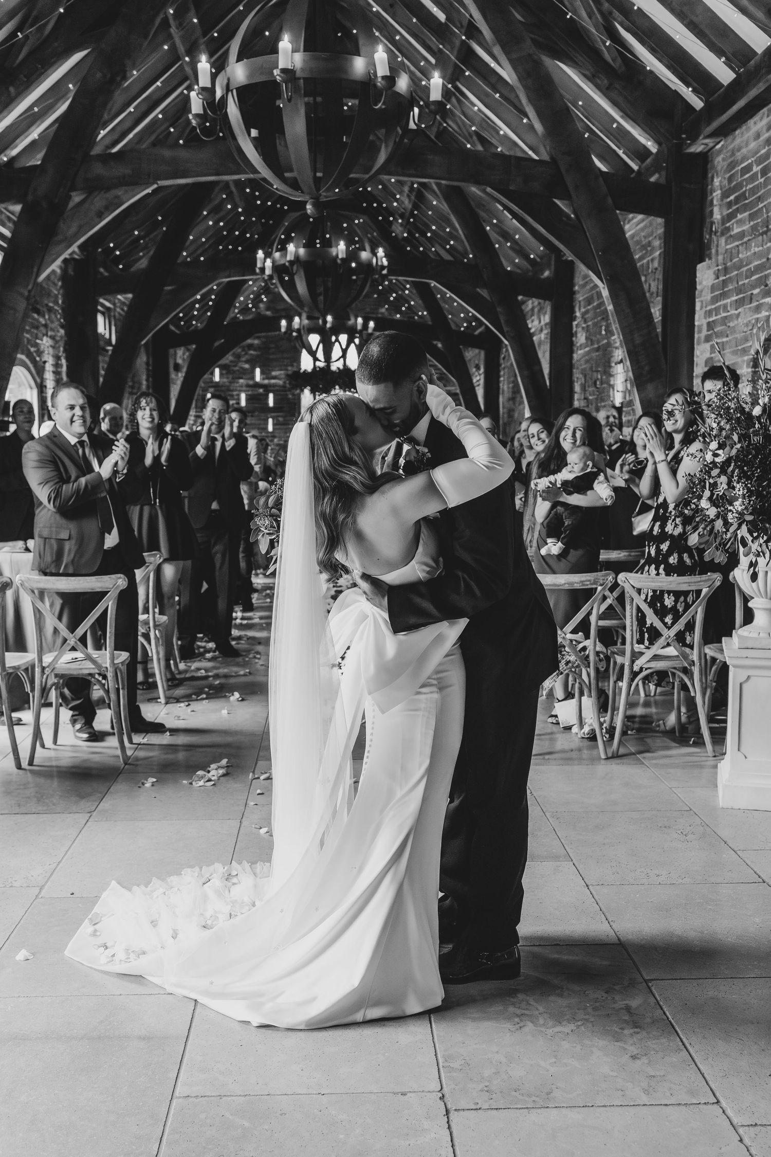 Black and white photo of first dance in rustic barn venue with exposed wooden beams.