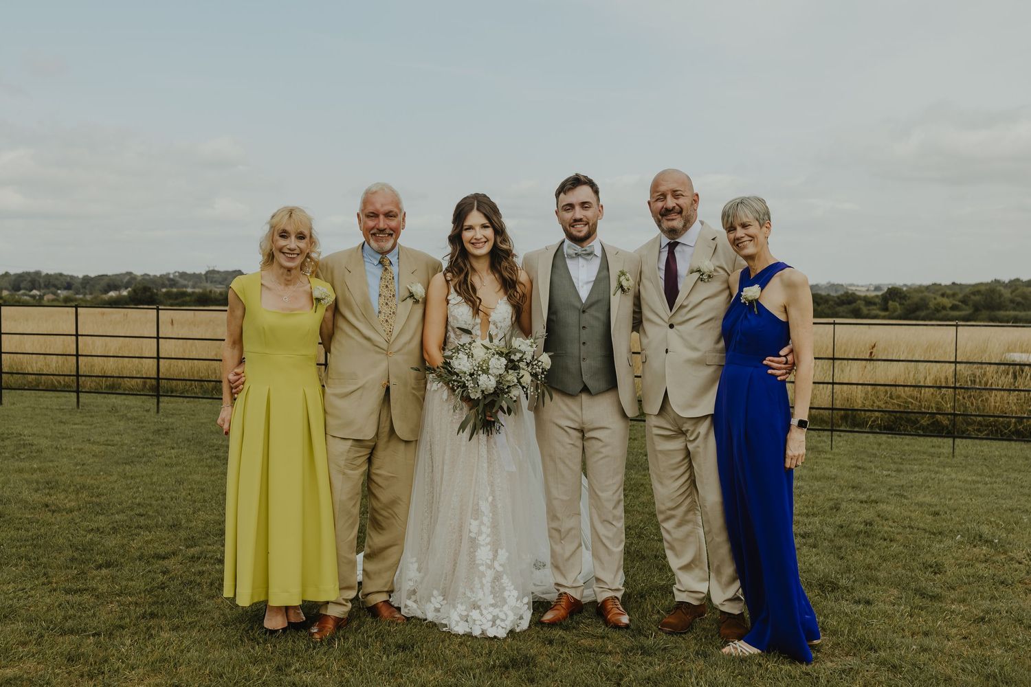 Family portrait on a rustic farm with wedding party members in formal attire.