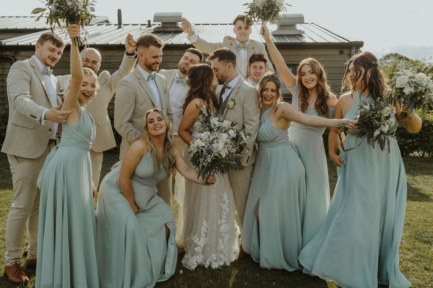 Candid moment of wedding party laughing together in mint green dresses and light suits.