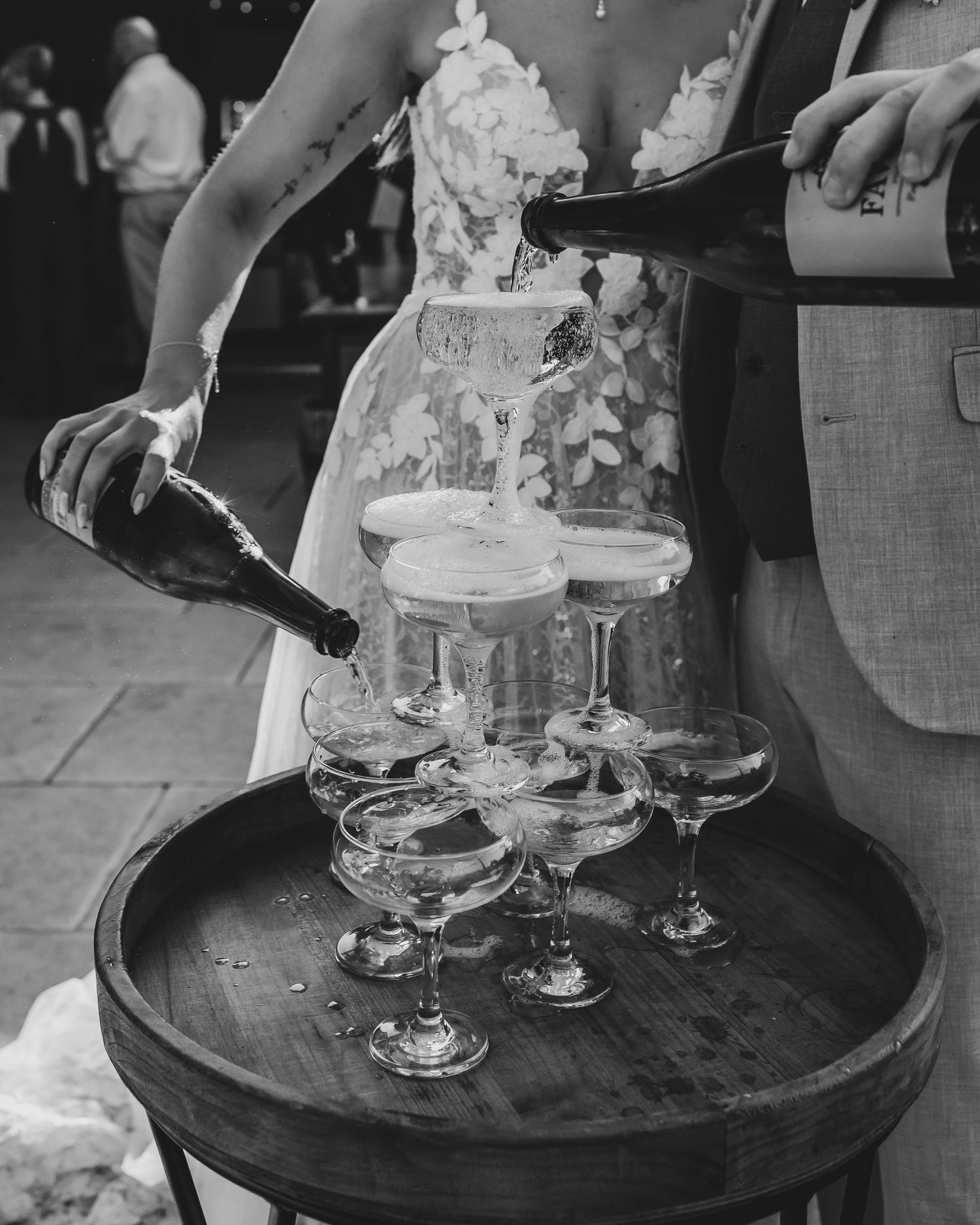 Wedding cake and champagne glasses arranged on dark wooden barrel tables.