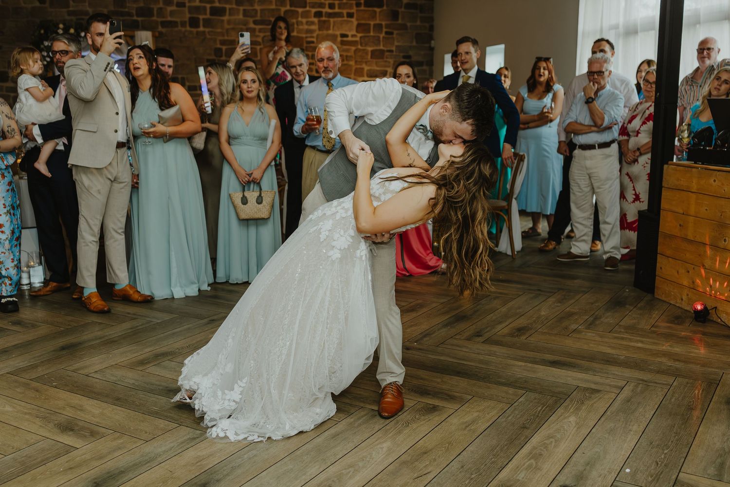 Wedding reception dance floor filled with guests celebrating in a rustic brick-walled venue.