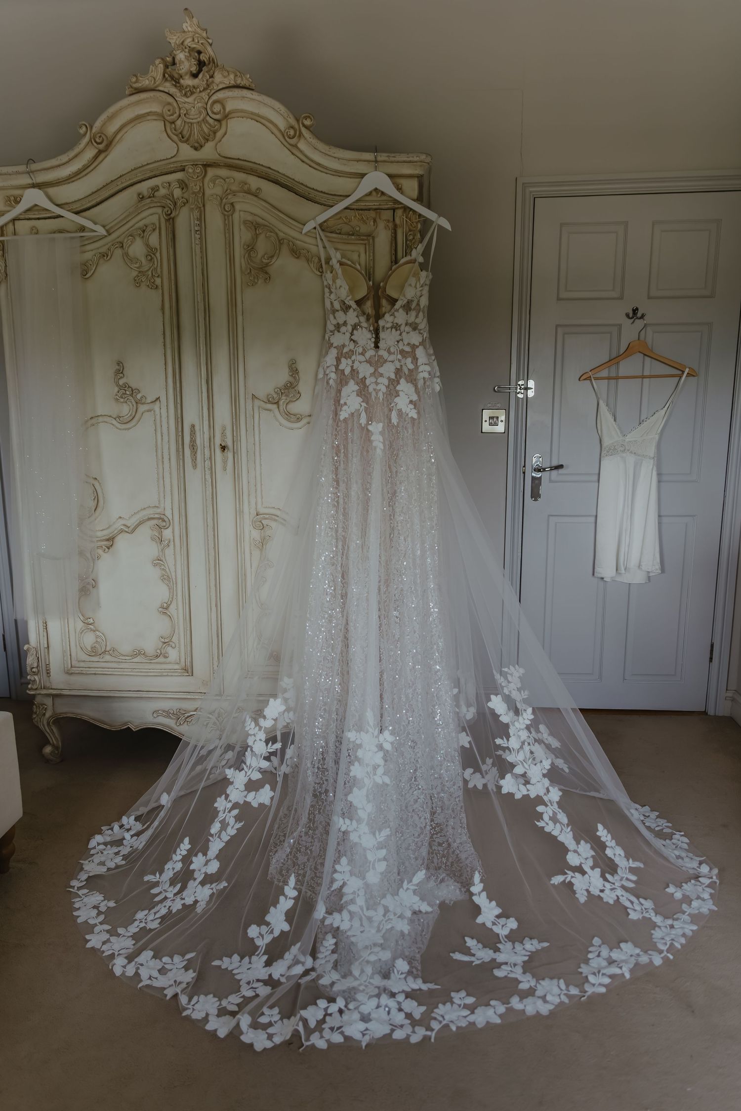 Ornate white wedding dress with lace train displayed in elegant room.